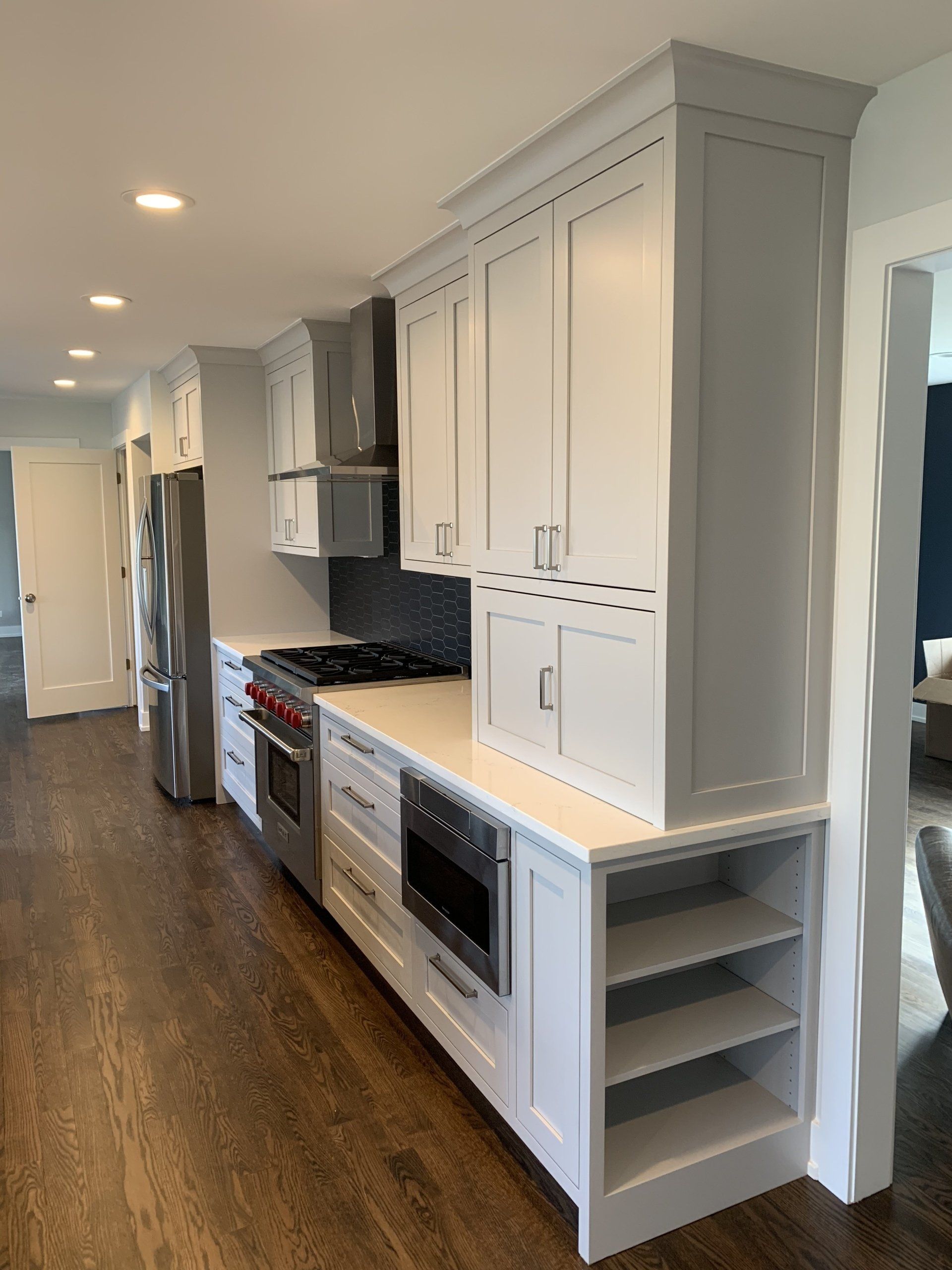 Modern kitchen with light gray cabinets, stainless steel appliances, and dark wood floors.