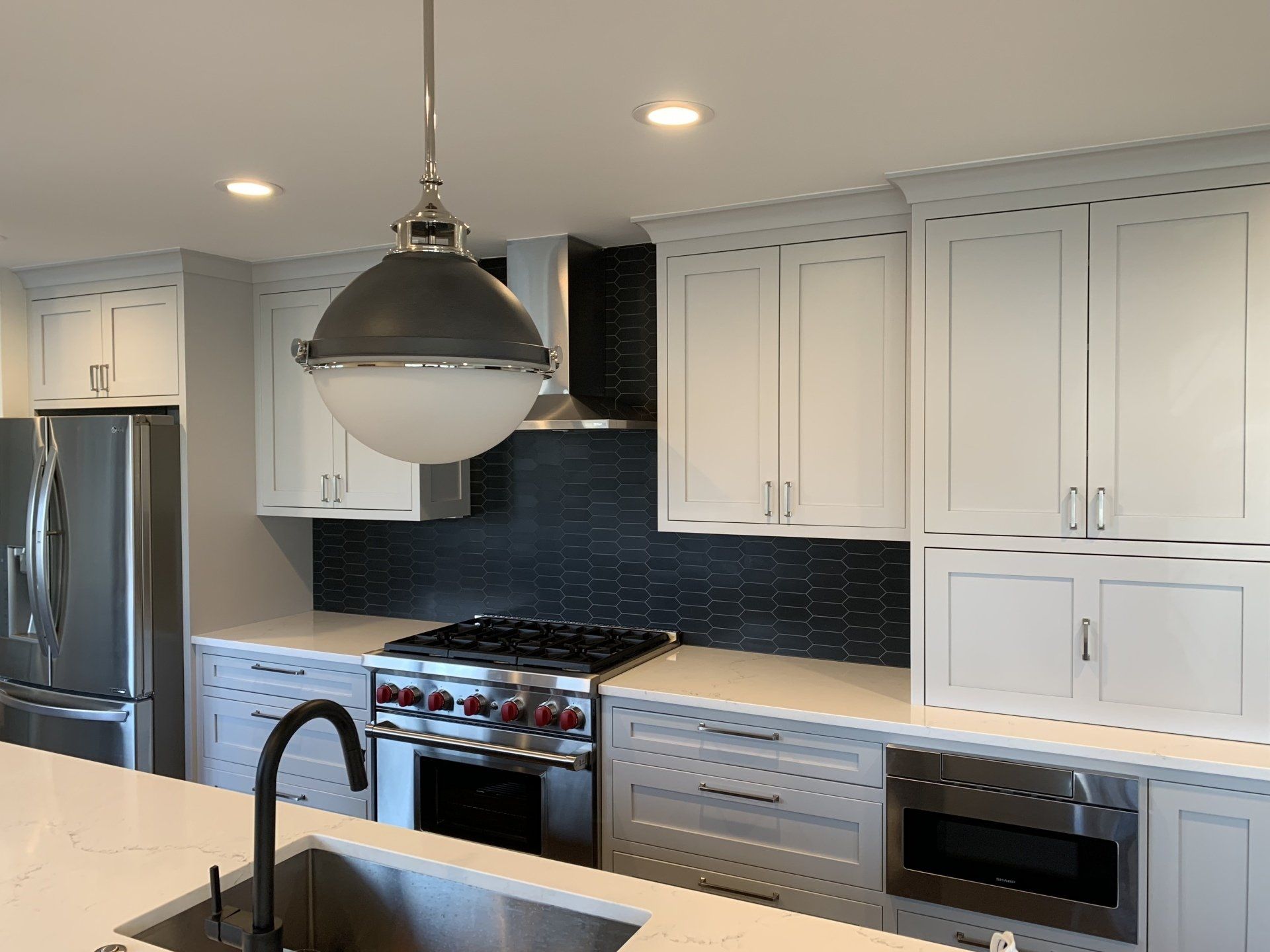 Modern kitchen with gray cabinets, stainless steel appliances, and a large pendant light.