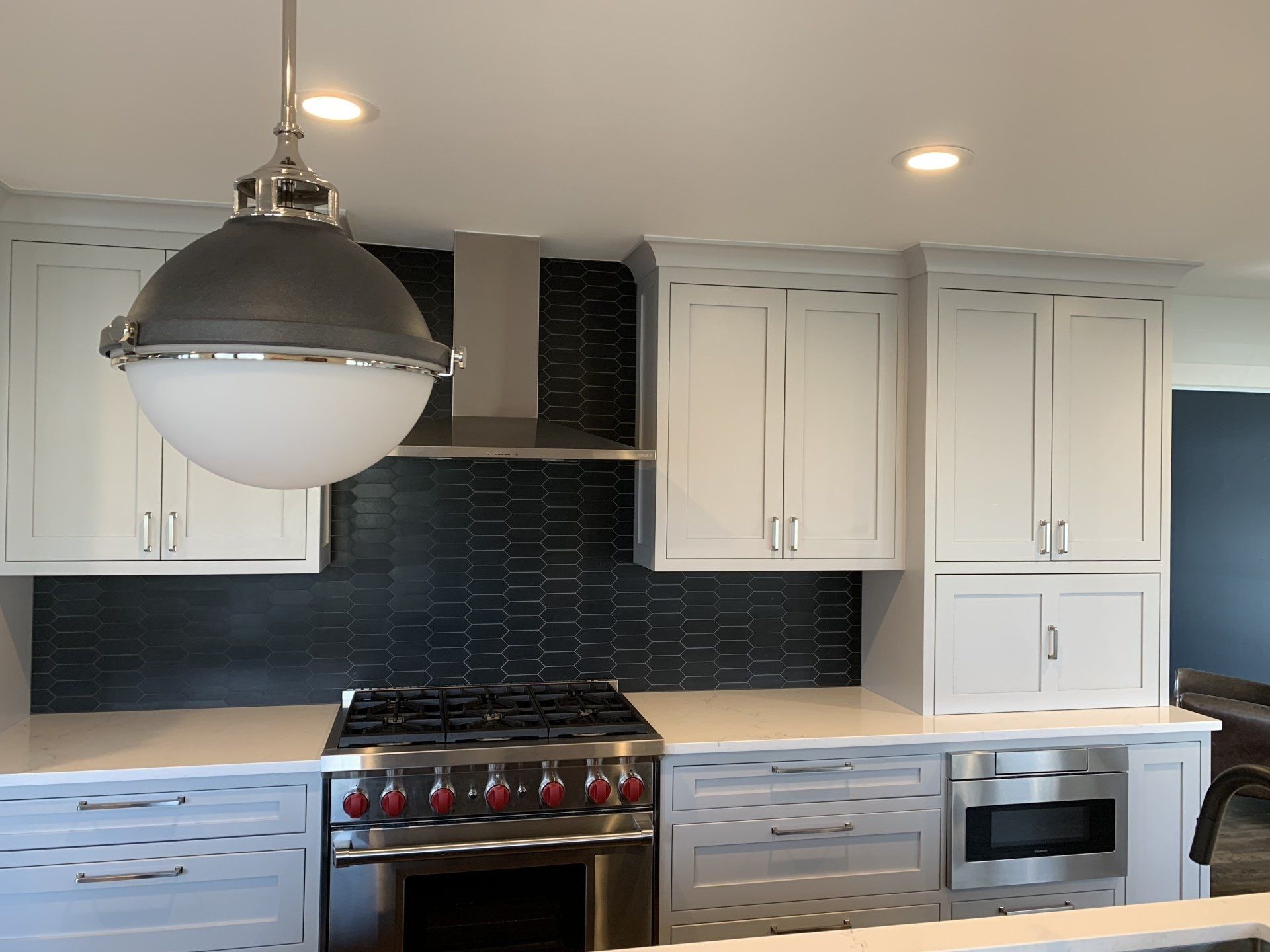 Gray kitchen with light cabinets, dark backsplash, and a large pendant light.