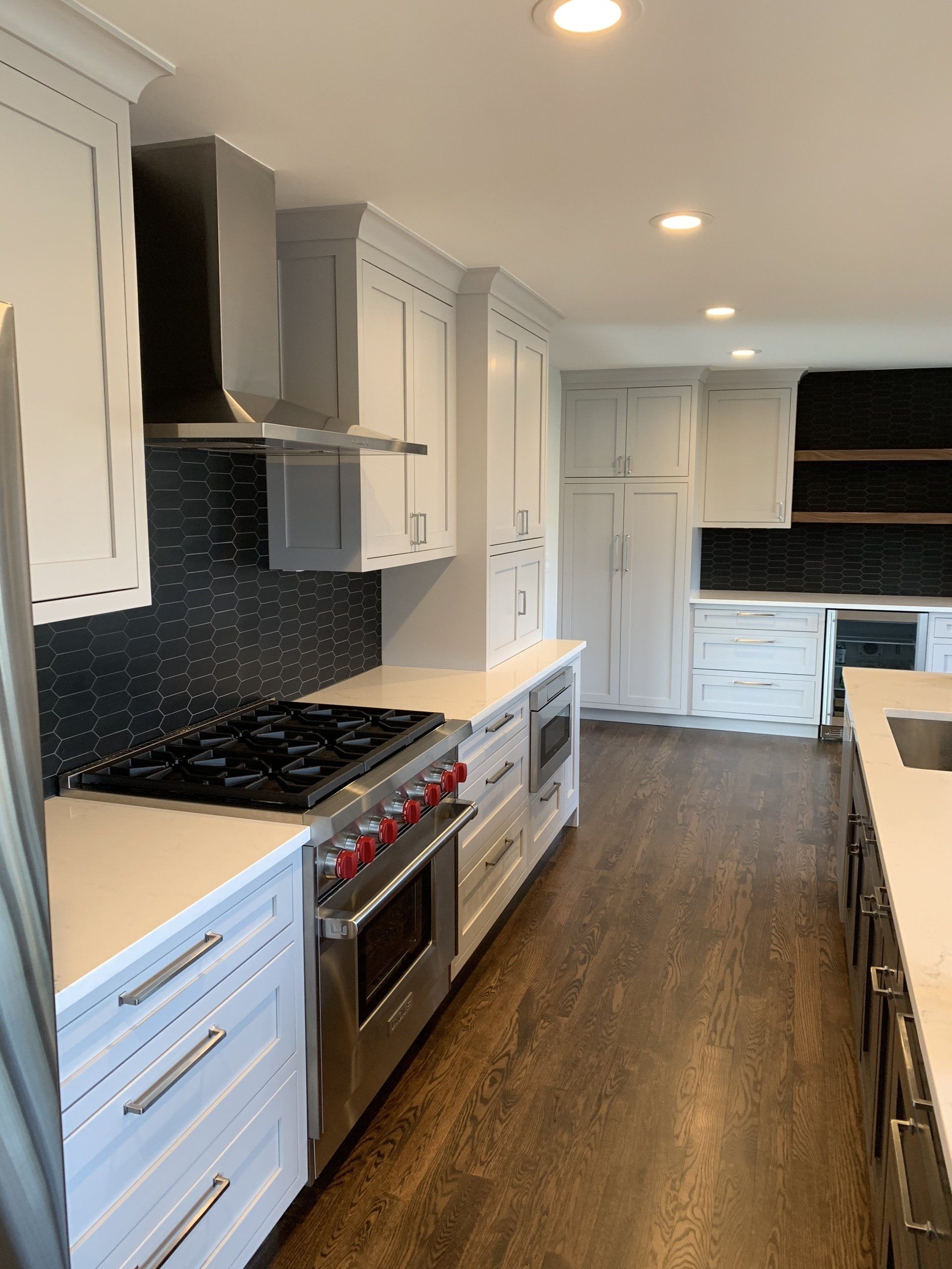 Modern white kitchen with stainless steel appliances, dark backsplash, and hardwood floors.