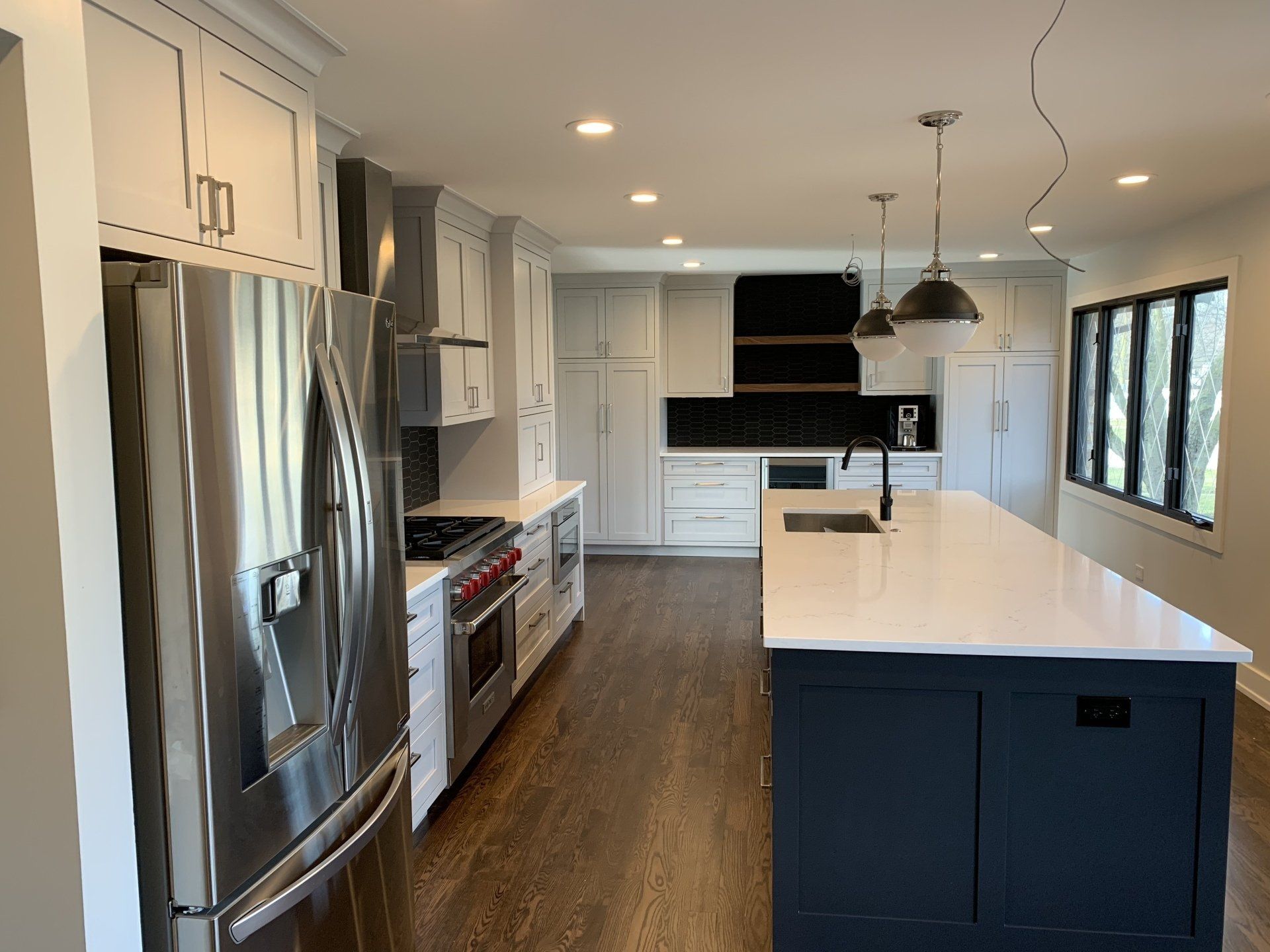 Modern kitchen with white and dark blue cabinetry, stainless steel appliances, and dark hardwood floors.