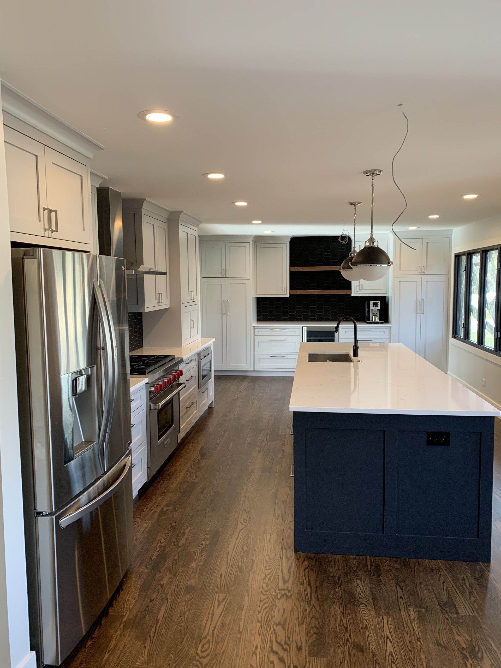 Modern kitchen with navy island, white countertops, stainless steel appliances, and dark wood floors.