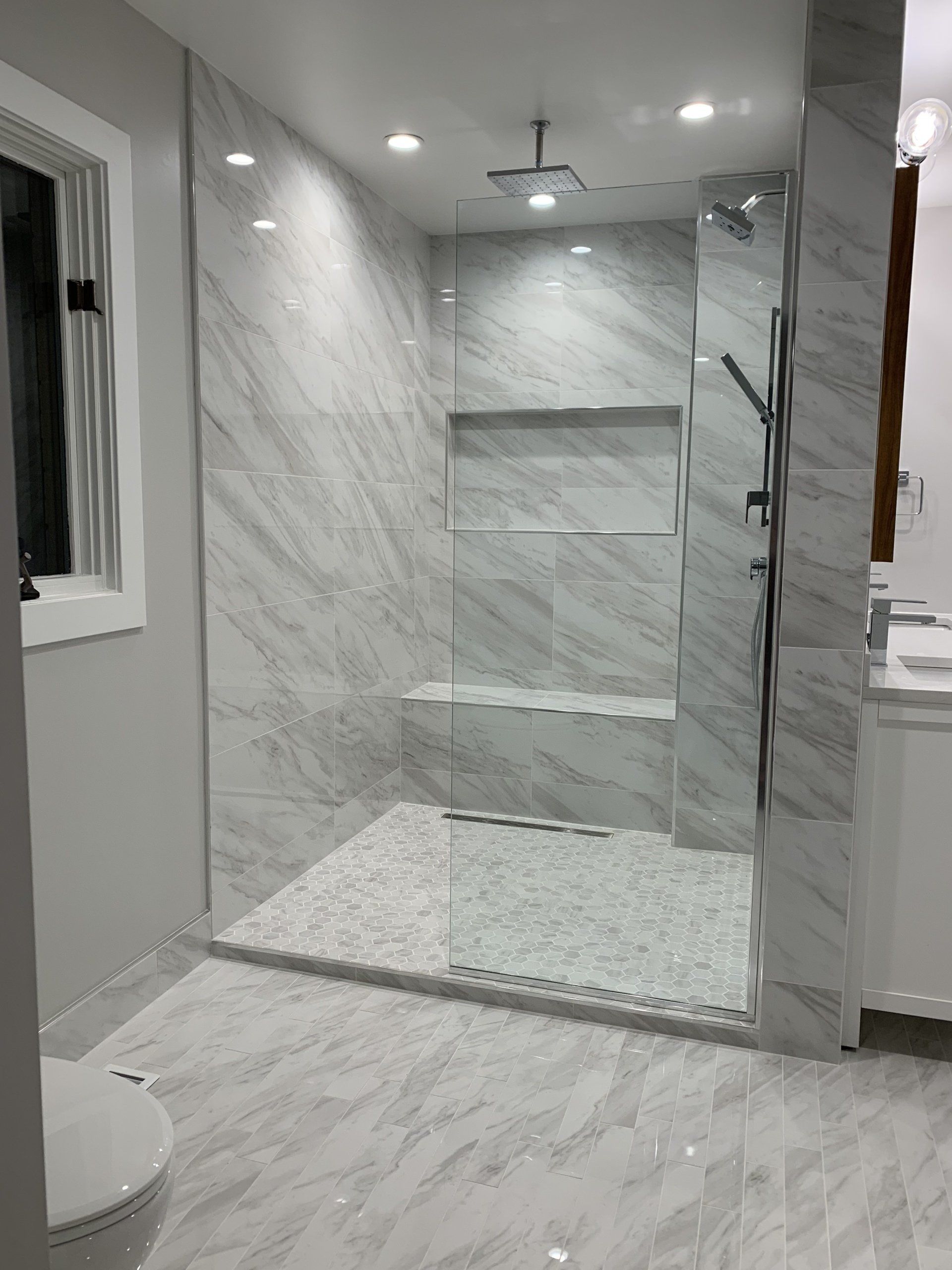 Spacious modern bathroom with a walk-in shower featuring gray marble tile and pebble floor.
