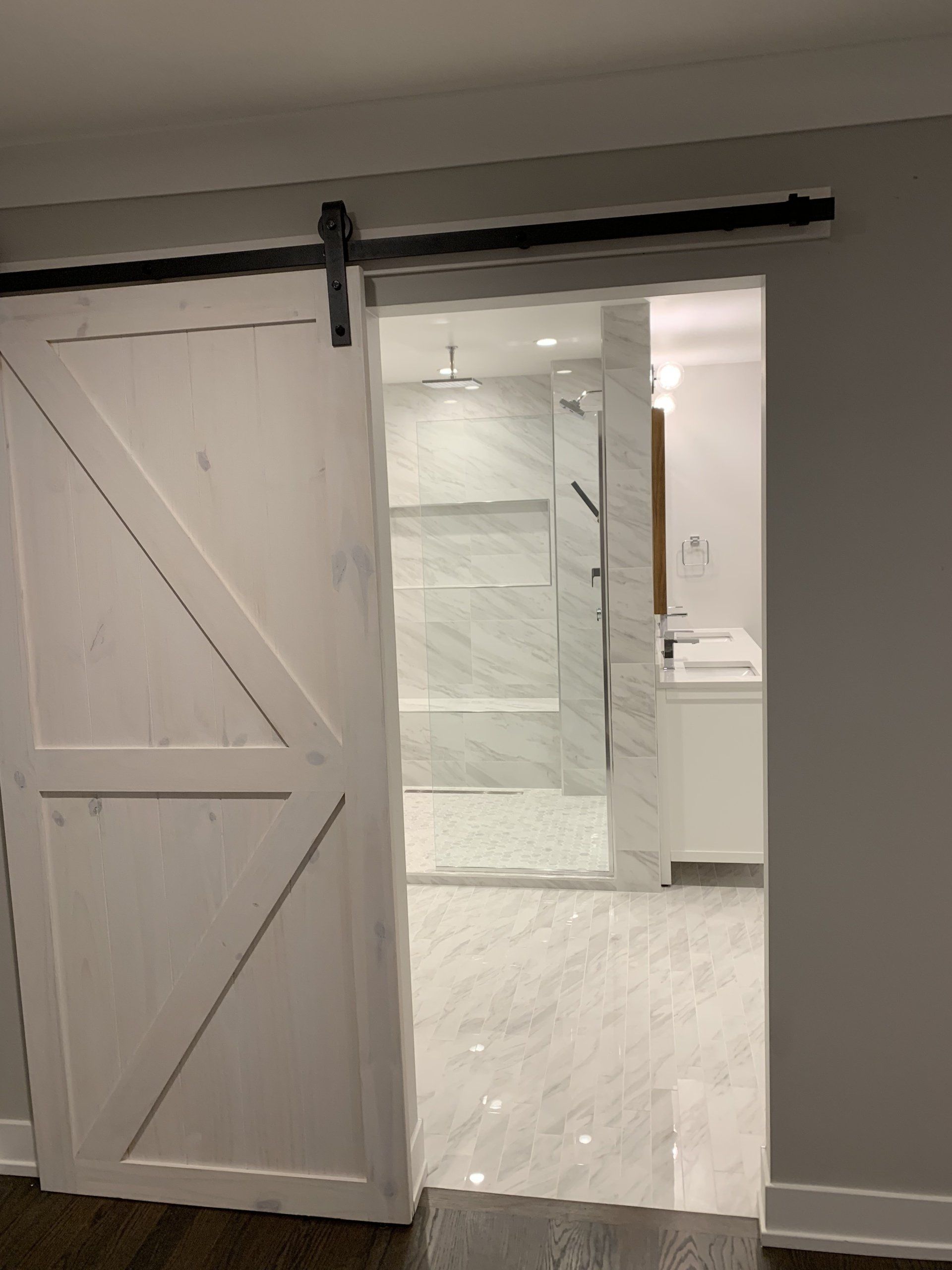 White barn door open to a modern bathroom with marble tile and shower.