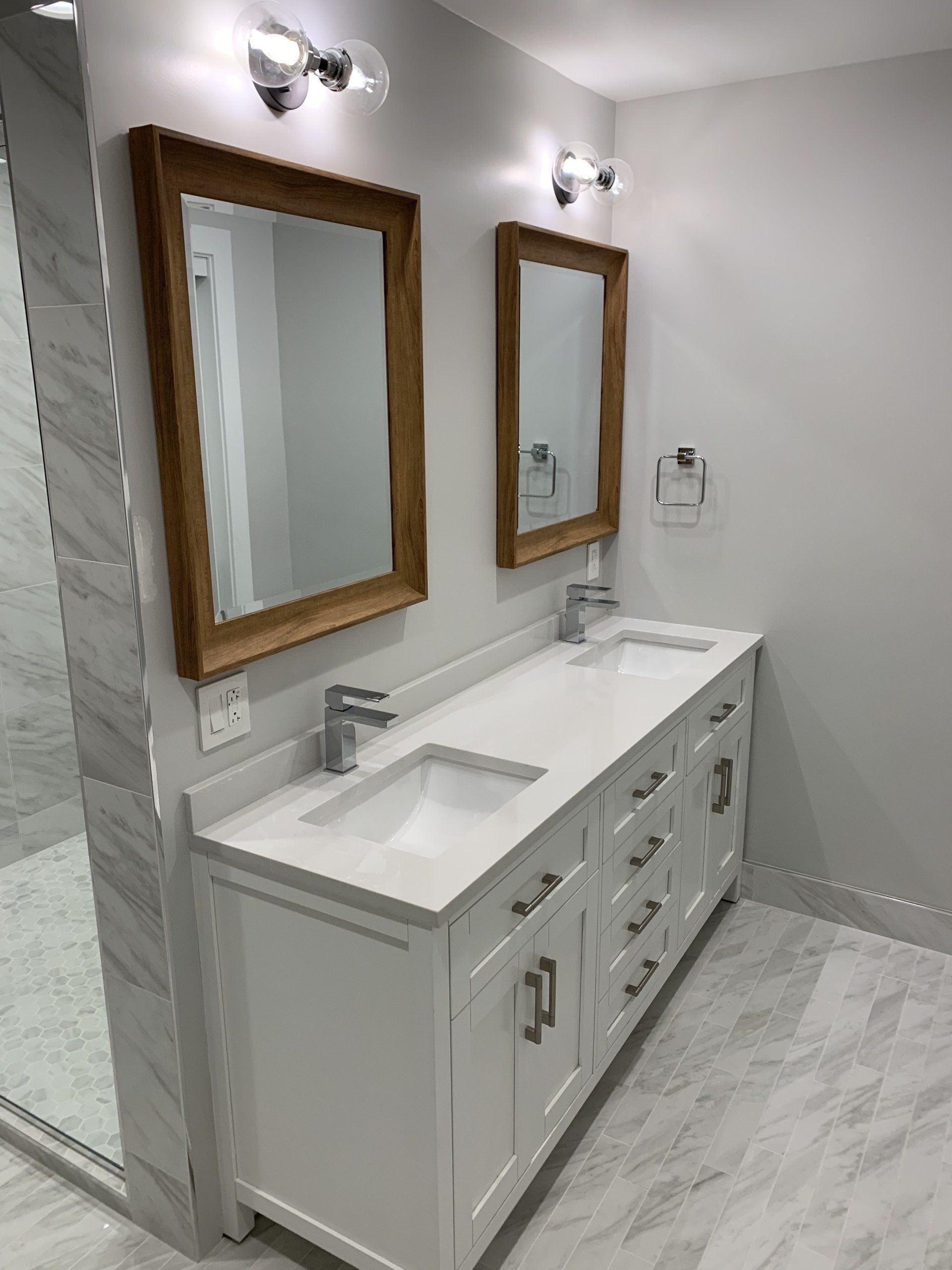 Bathroom with white double vanity, wooden framed mirrors, and marble flooring.