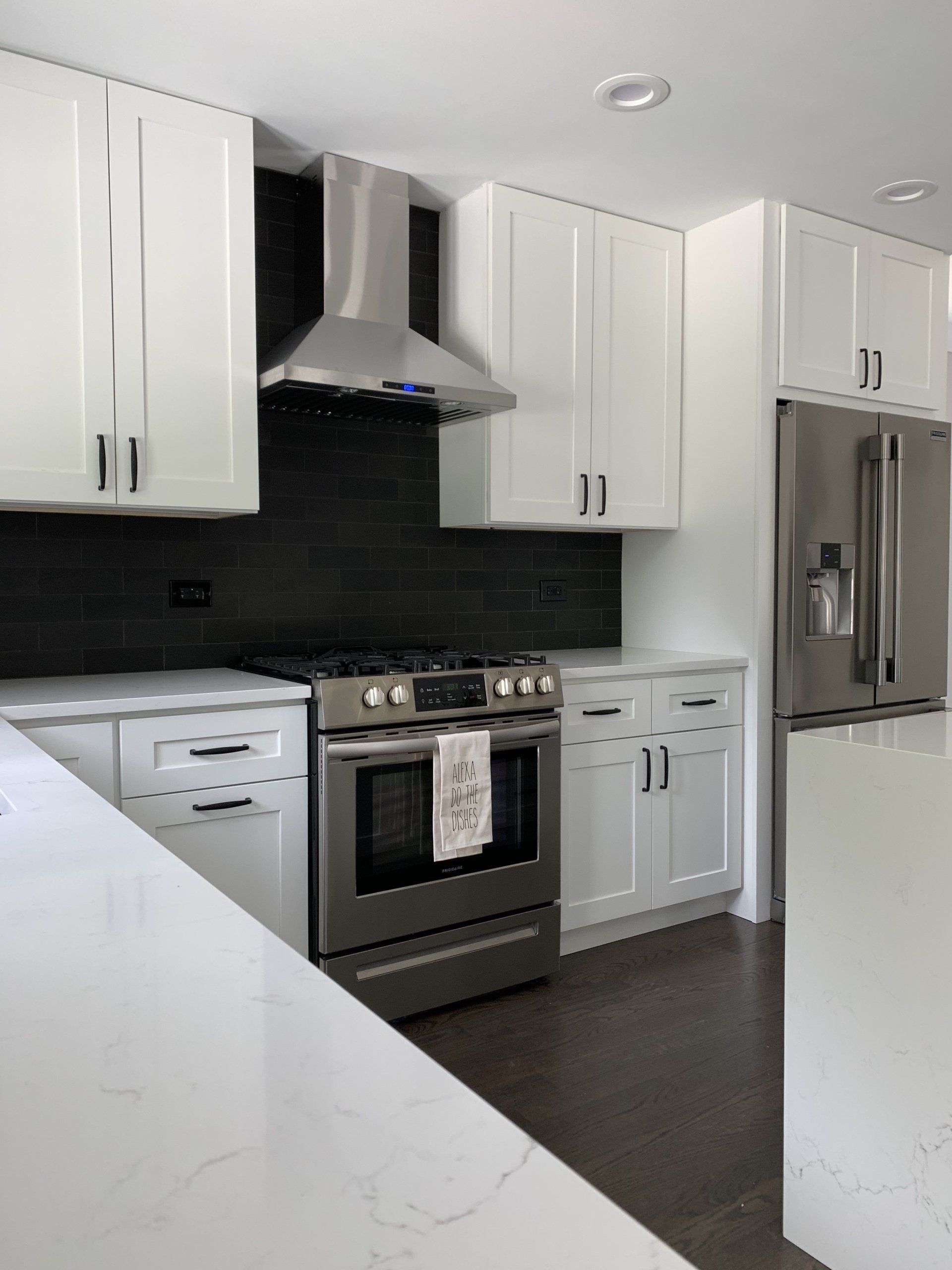 Modern white kitchen with stainless steel appliances and dark backsplash.