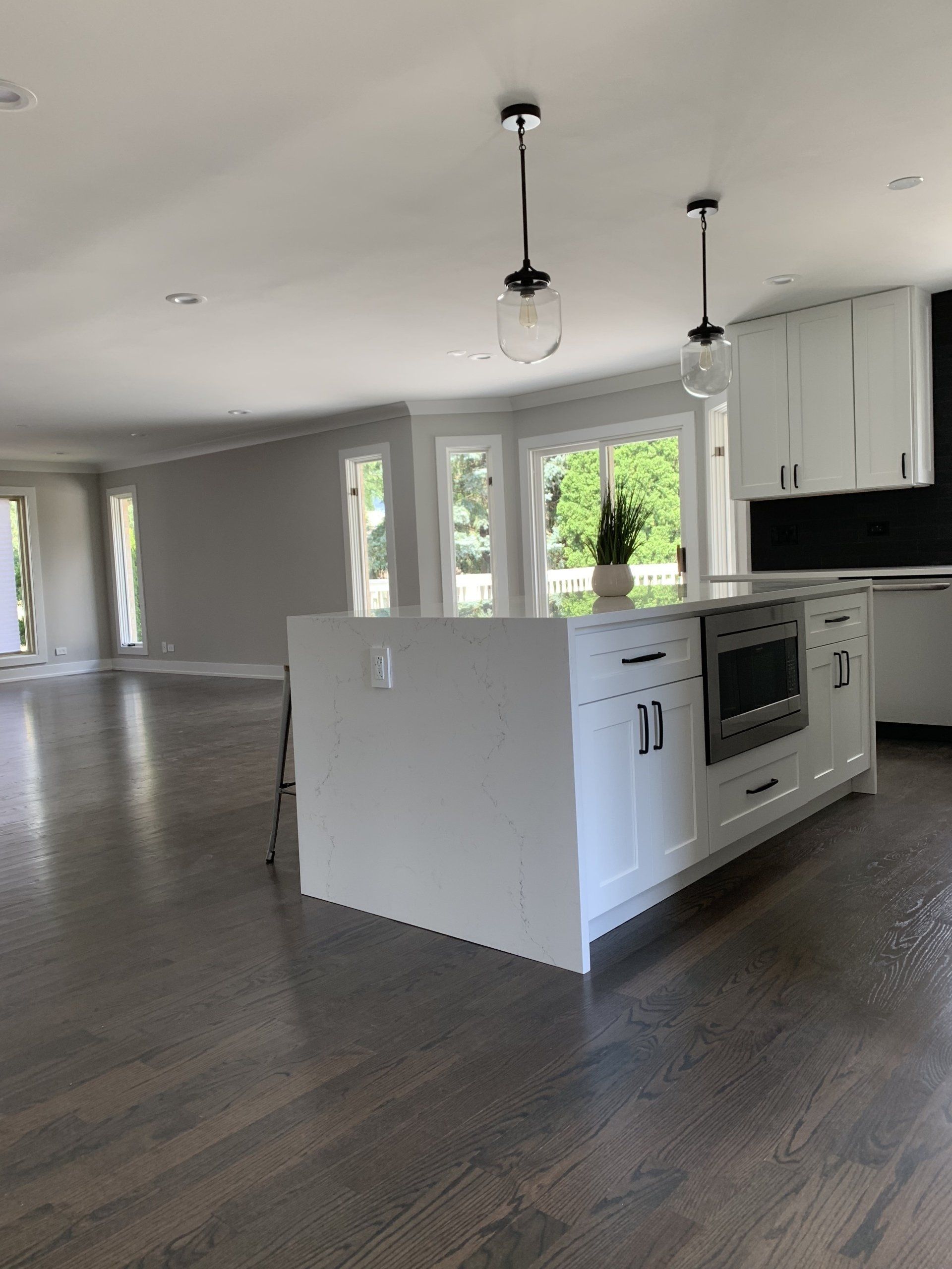 Spacious white kitchen with island, built-in oven, dark wood floors, and pendant lights.