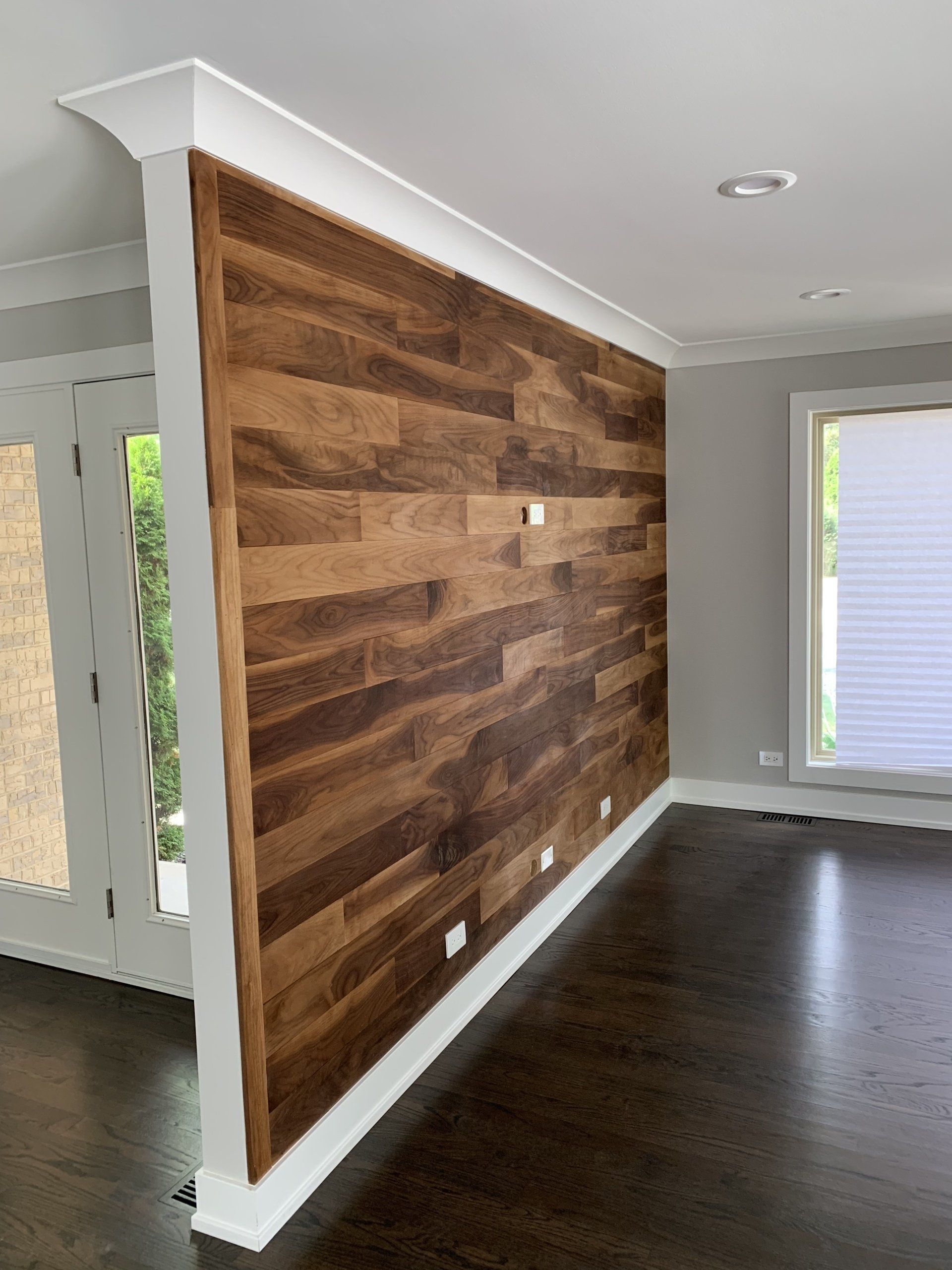 Wooden accent wall with white trim, in a room with dark hardwood floors and a window.