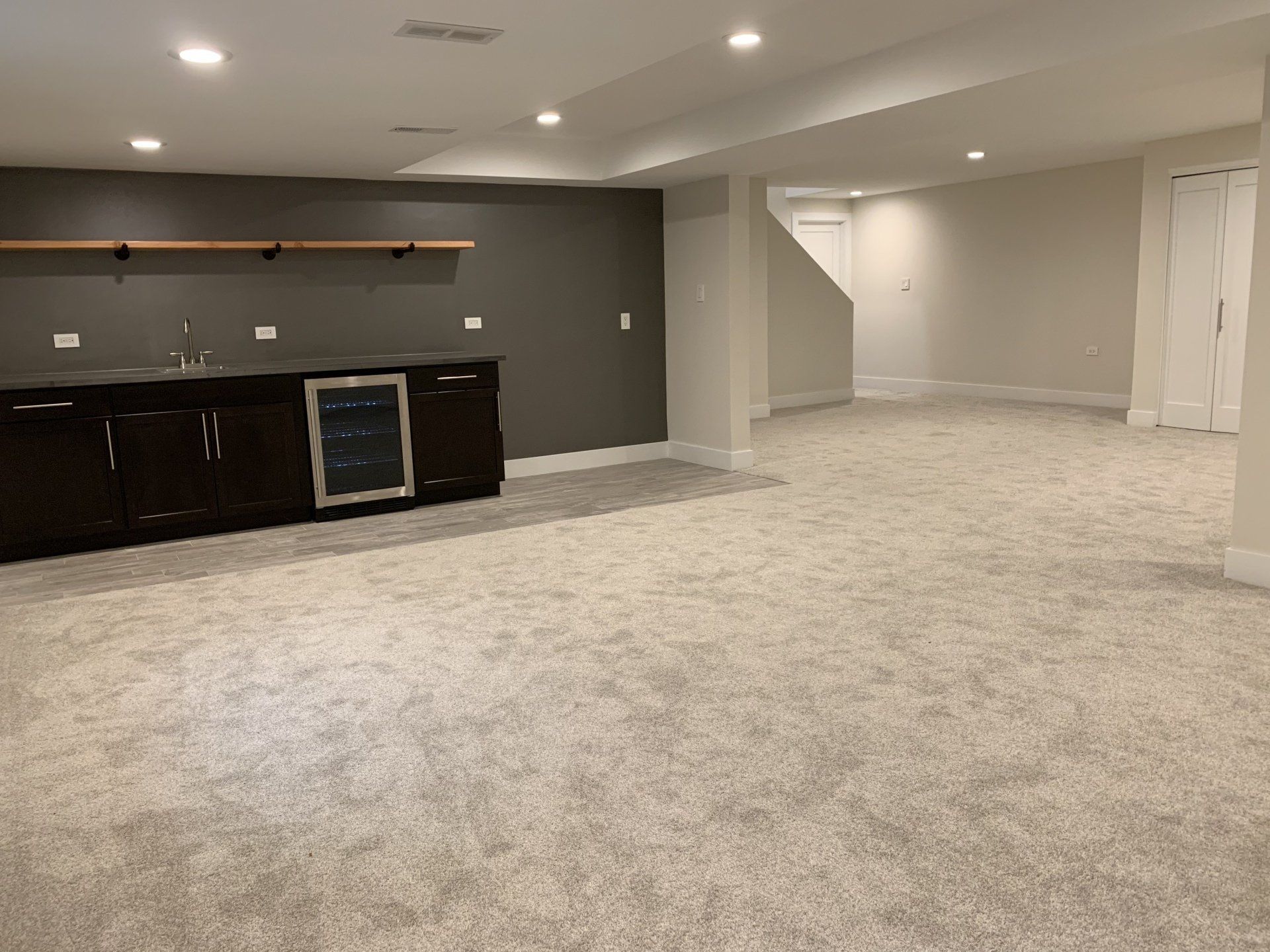 Empty basement with a bar area, neutral-colored carpet, and stairs leading up.