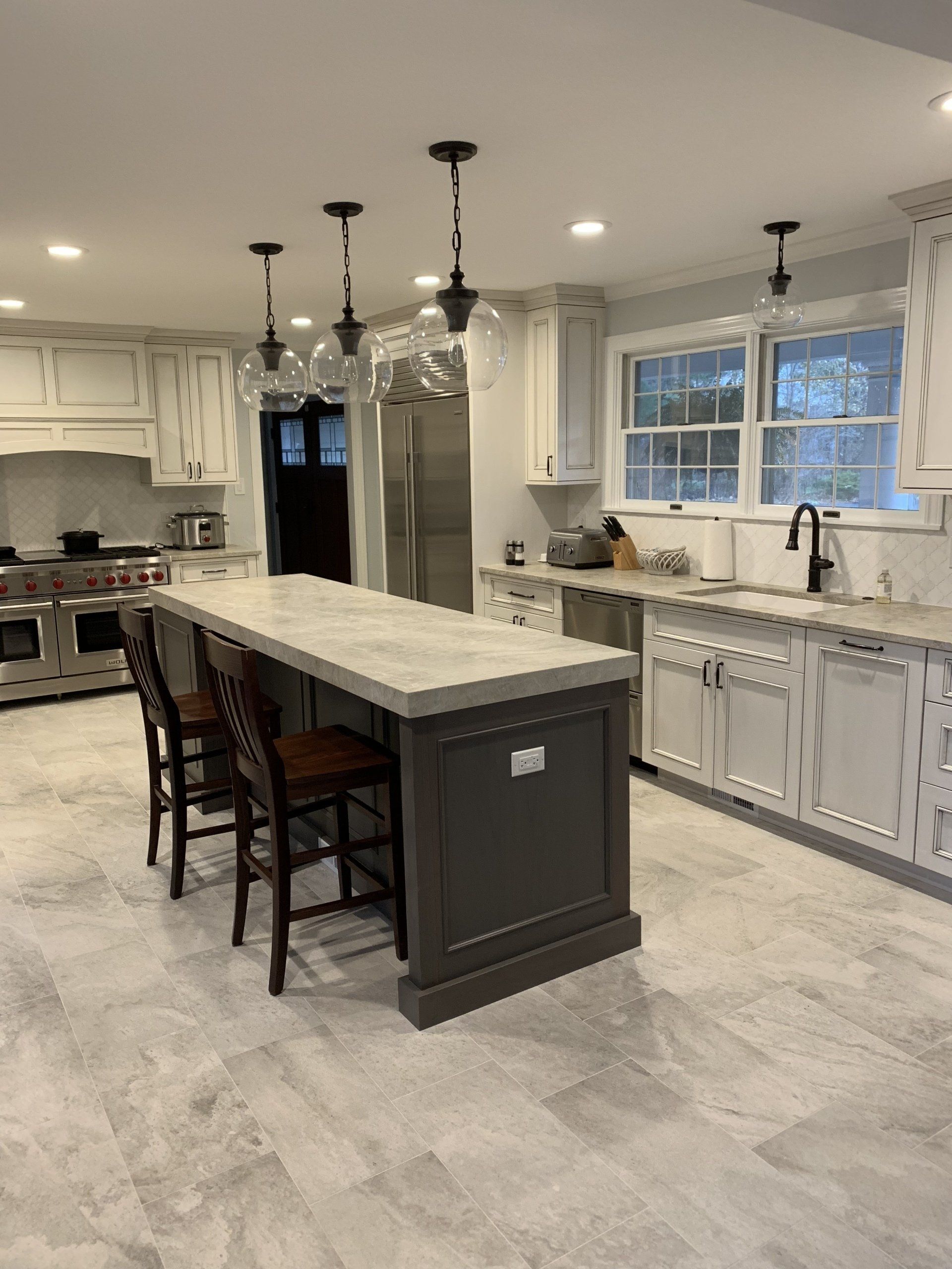 Modern kitchen with a dark gray island, white cabinets, and three hanging globe lights.
