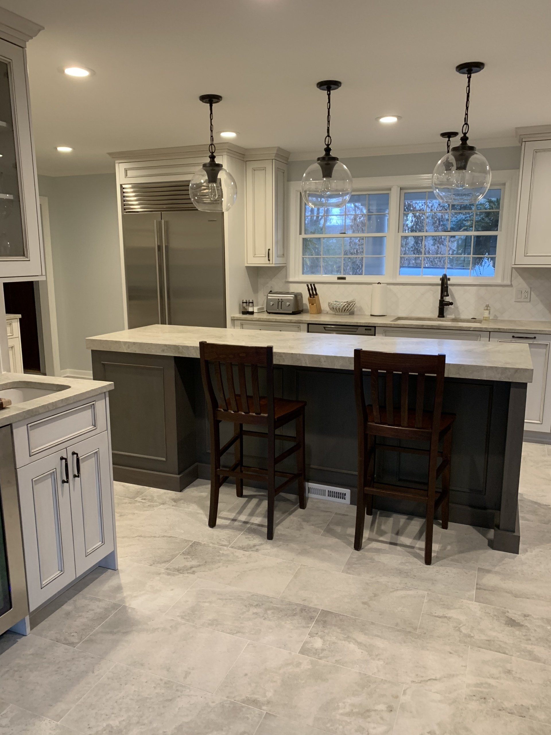Kitchen with an island, dark gray cabinets, light gray countertop, stools, and pendant lights.