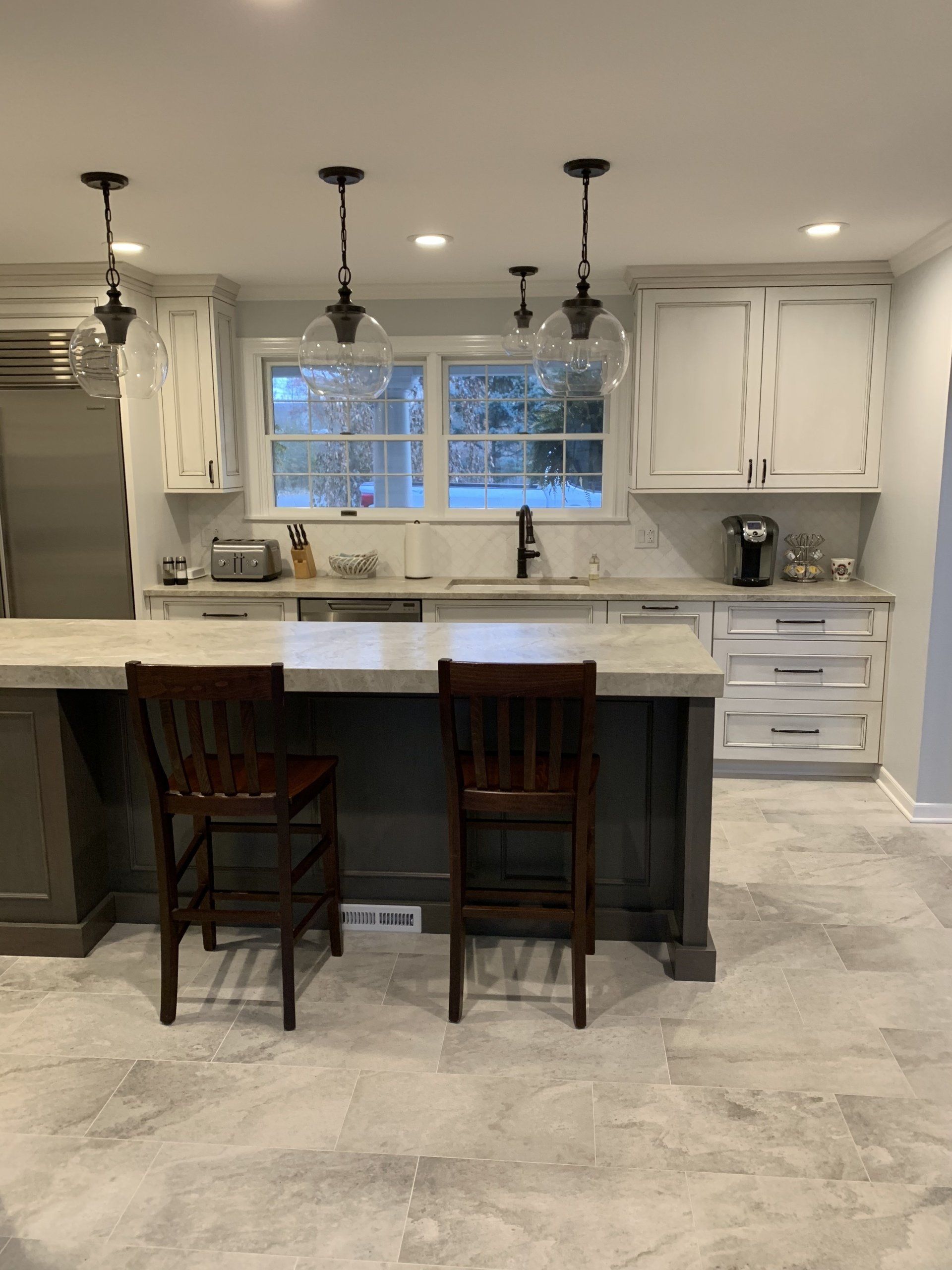 Kitchen with white cabinets, gray island, pendant lights, and two bar stools.