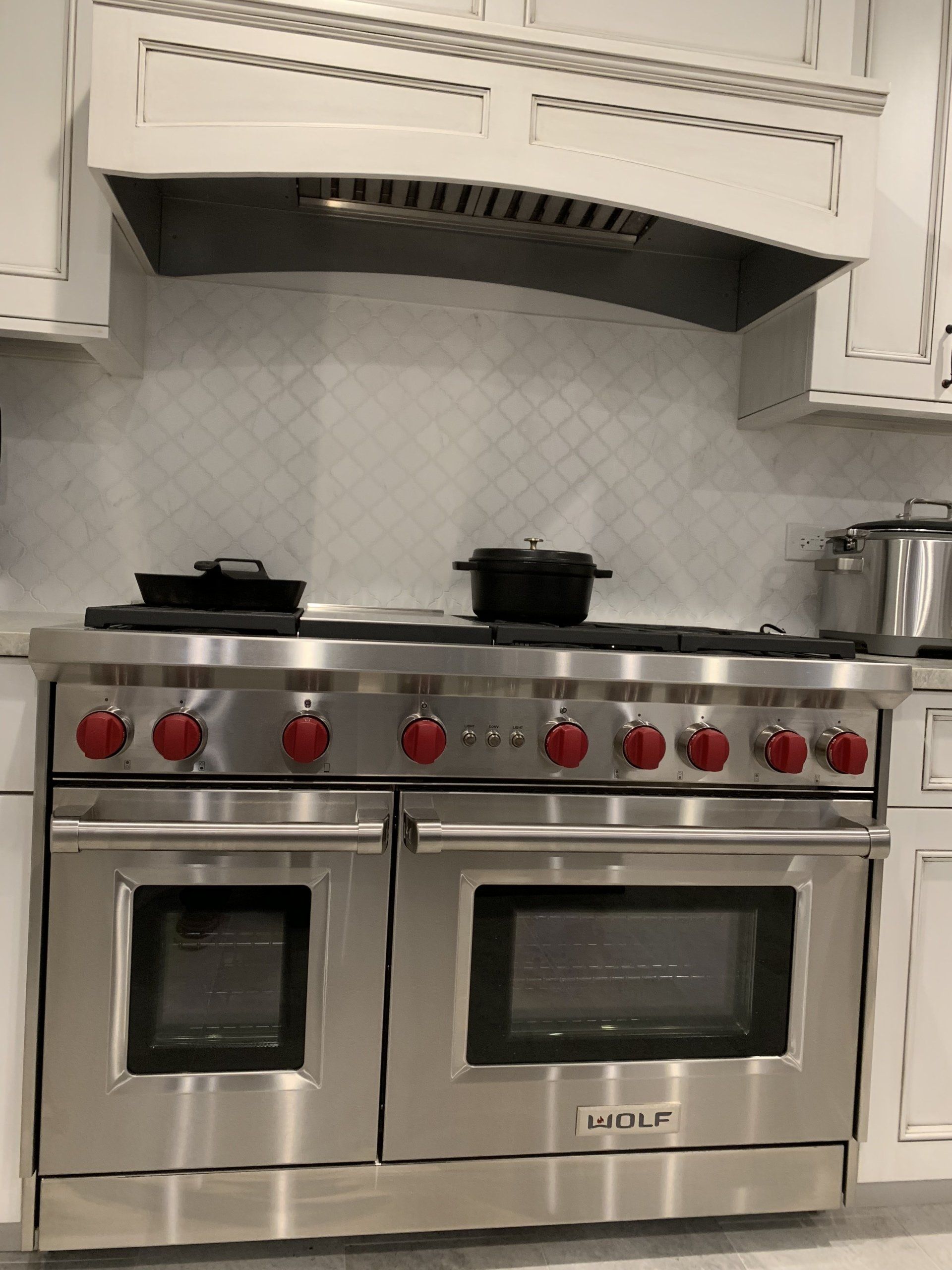Stainless steel Wolf range with red knobs, pots on stovetop, and white cabinets in a kitchen.