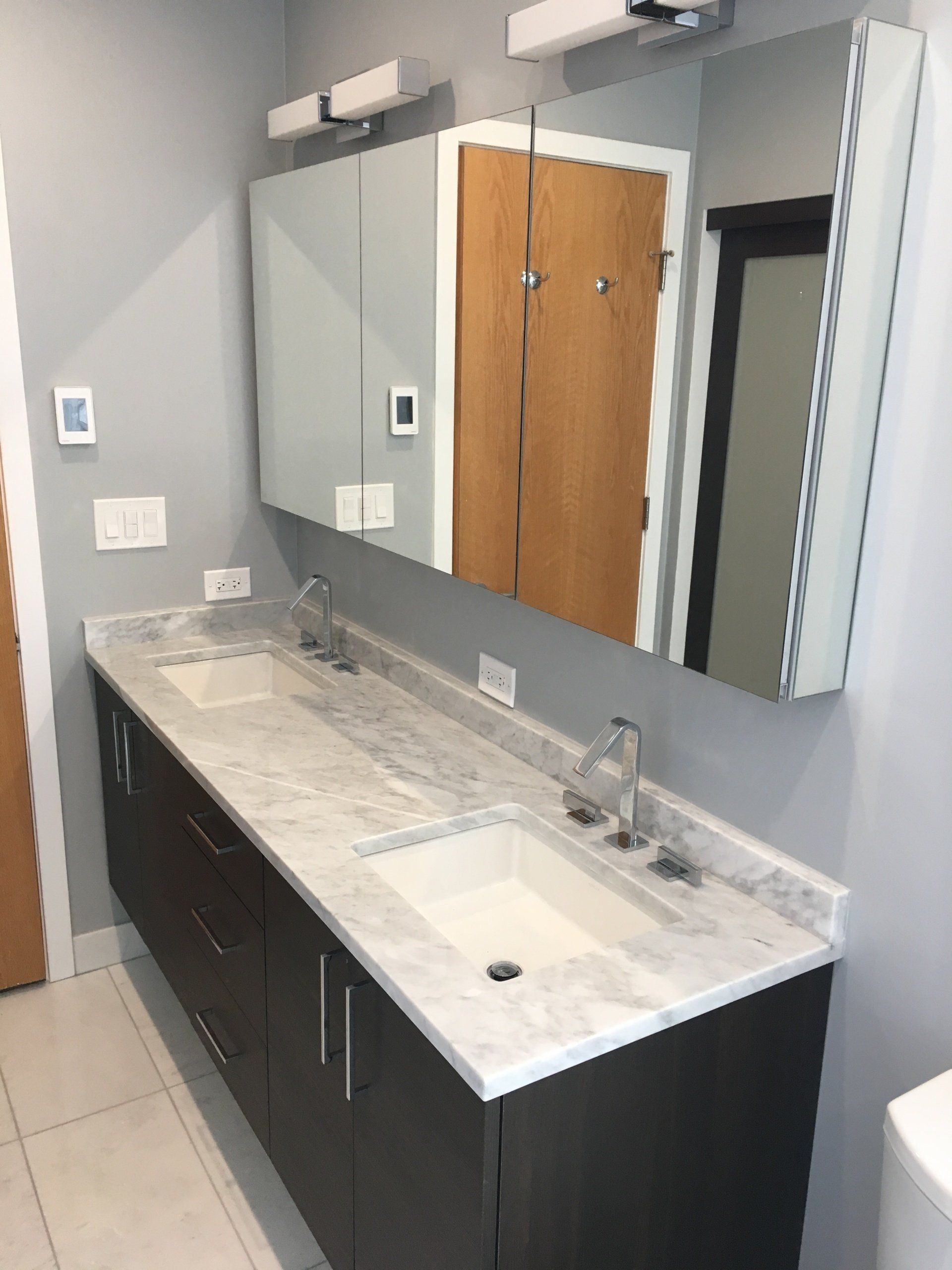 Bathroom with a double vanity, light gray walls, large mirror, and dark cabinets.