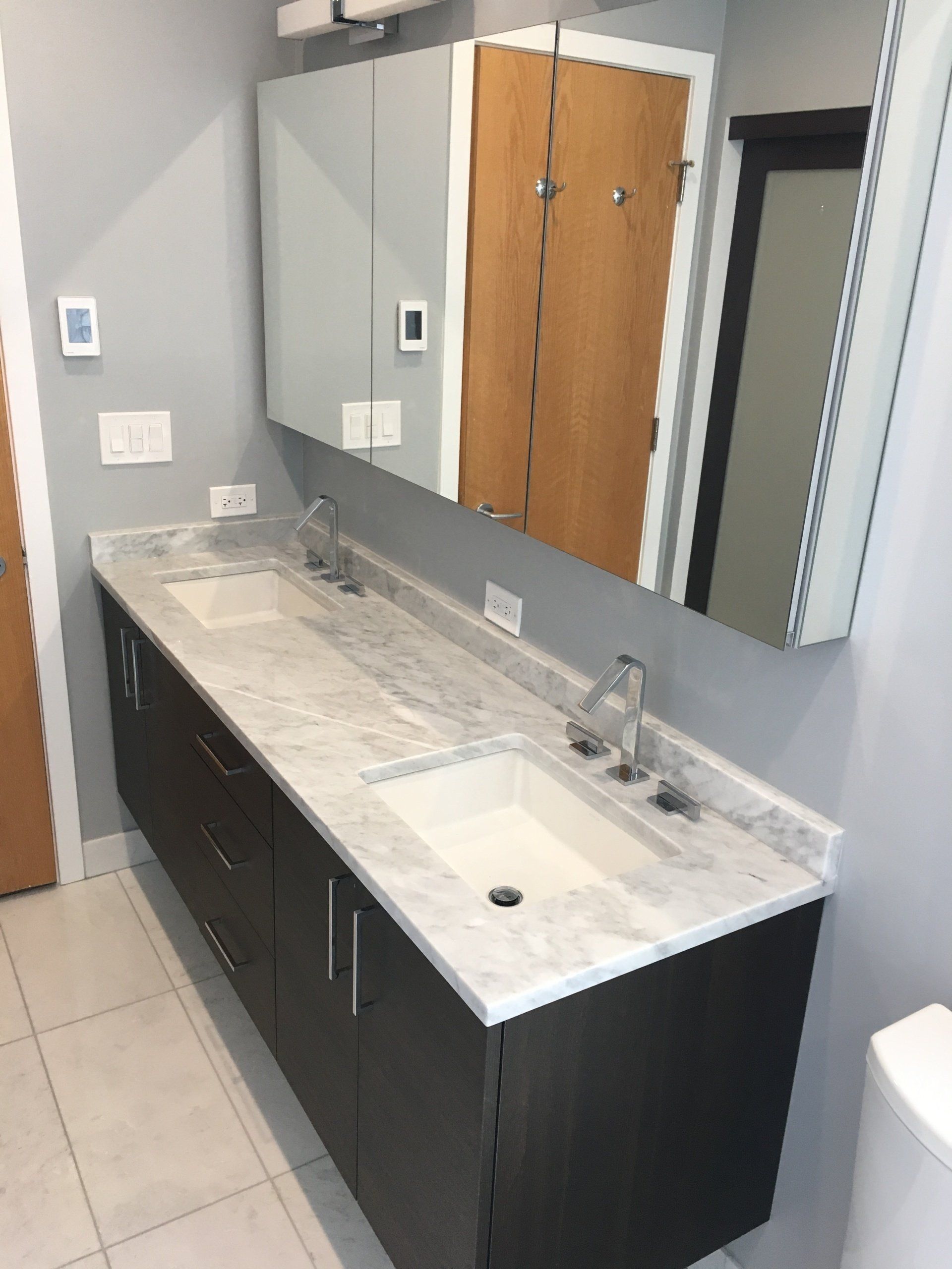 Modern bathroom with double vanity, marble countertop, dark cabinets, and large mirror.