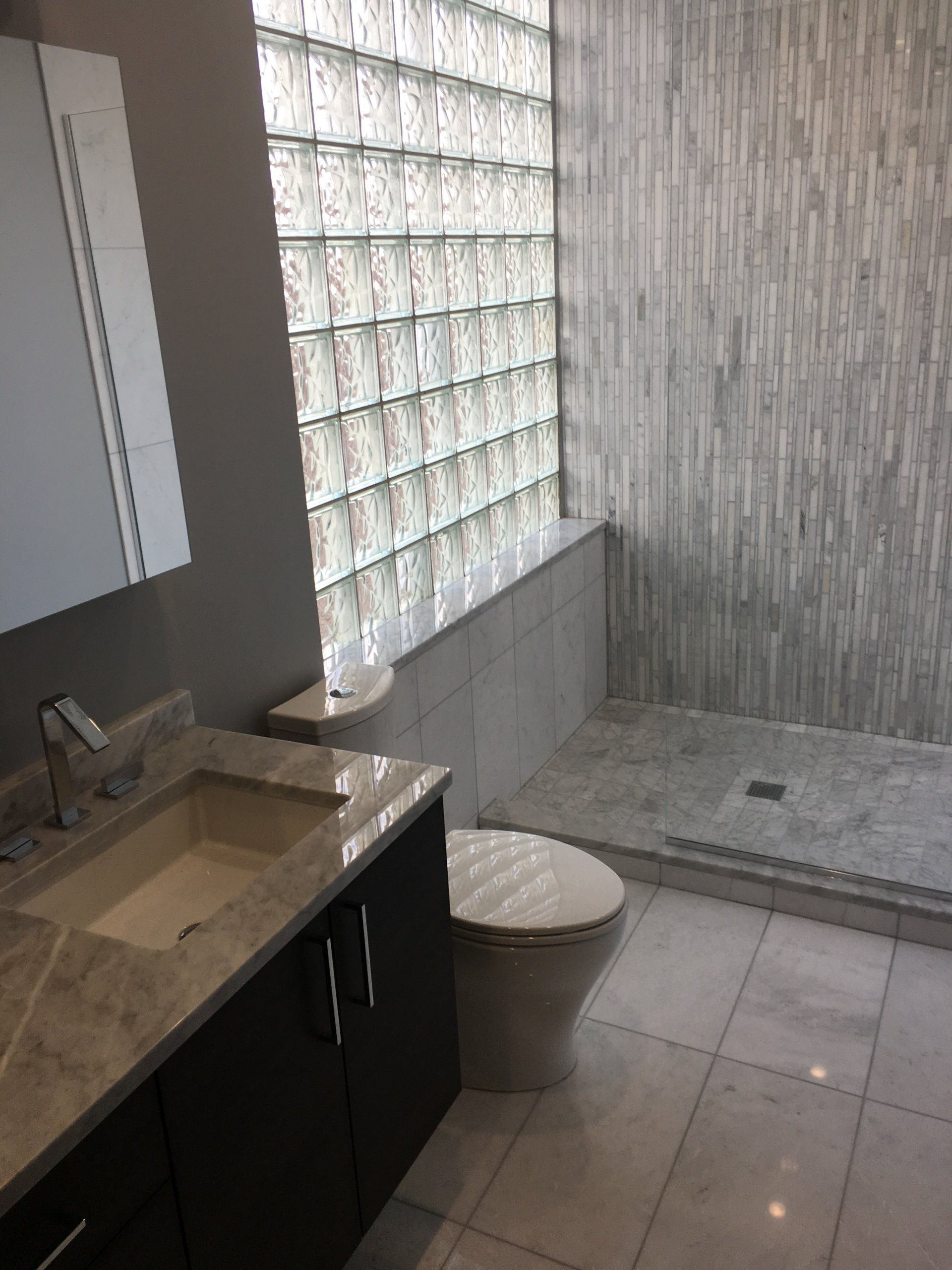 Bathroom with a glass block wall, marble countertop, and tiled shower.