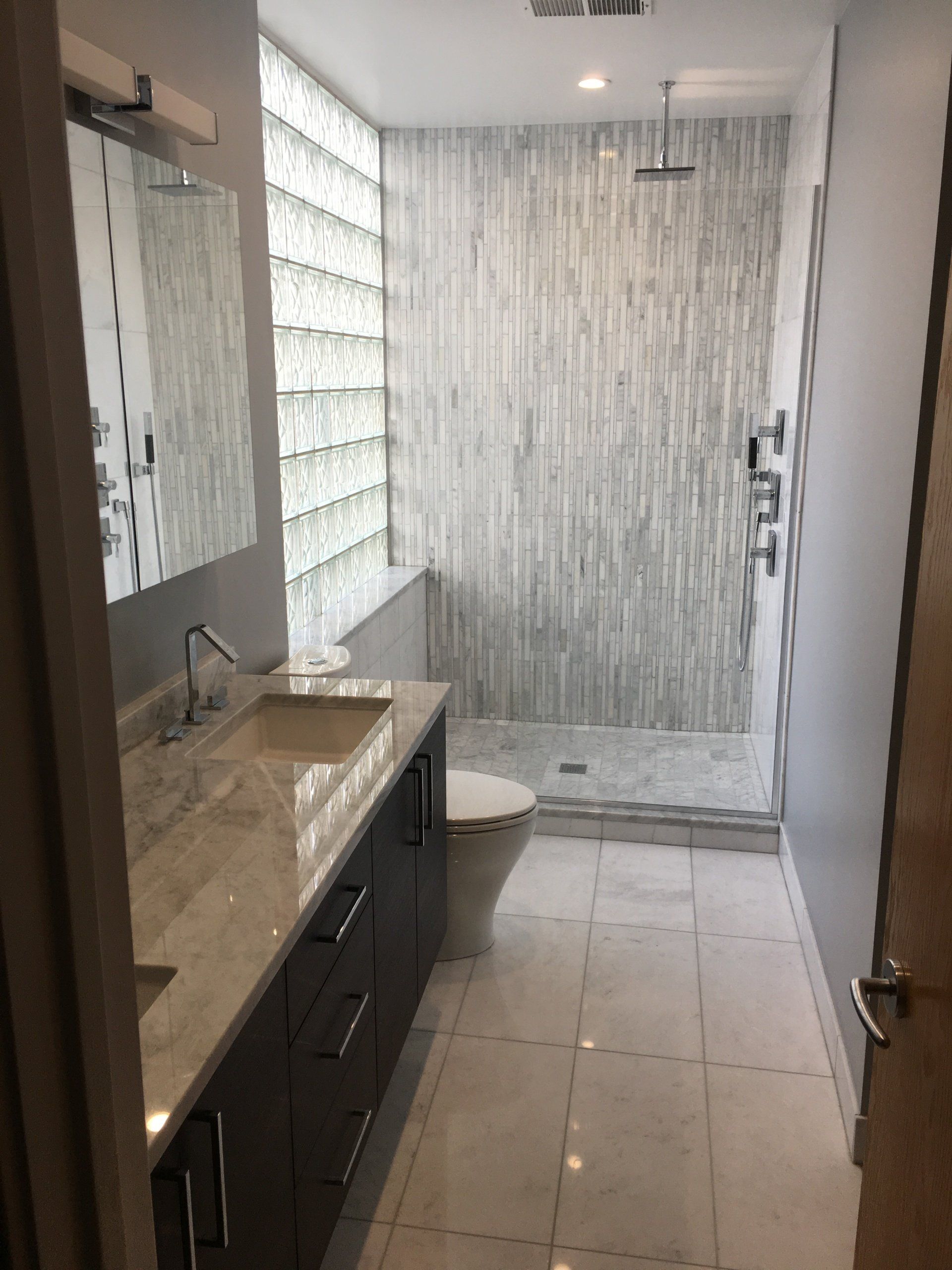 Modern bathroom with a glass block wall, vanity, toilet, and shower. Gray and white tones.