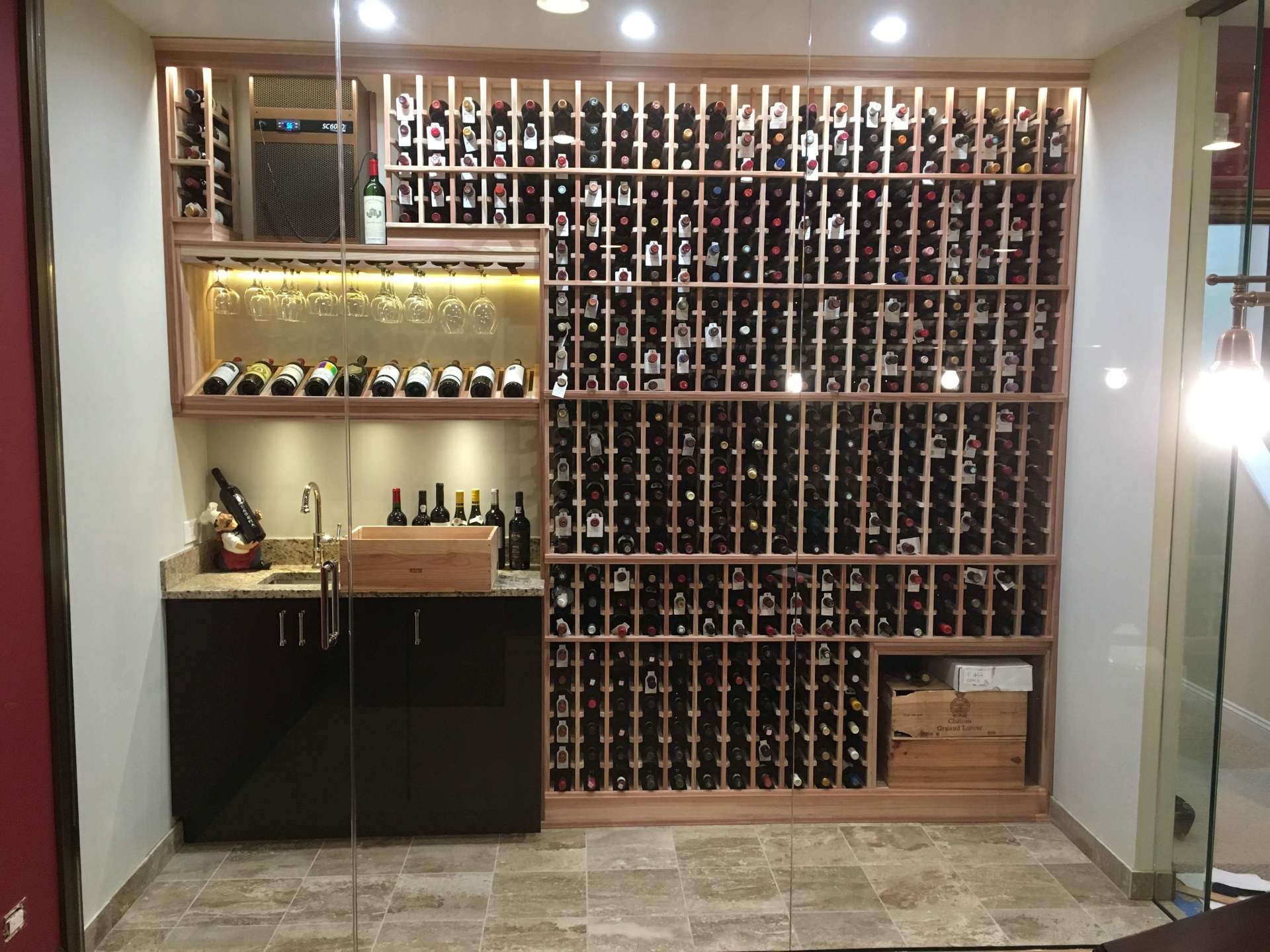 Wine cellar with wooden racks filled with wine bottles, bar area, and glass door.