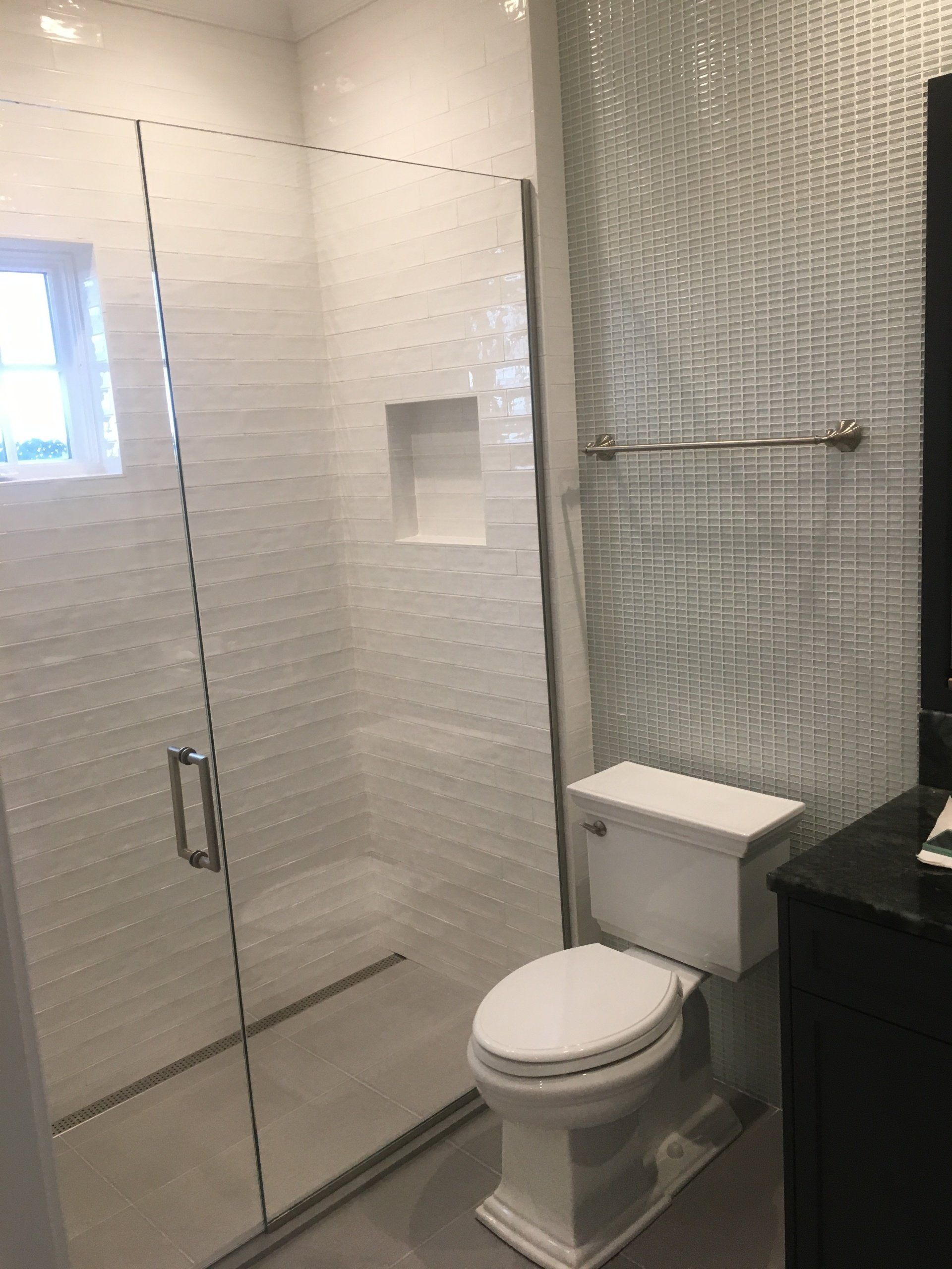 White-tiled bathroom with a glass shower, toilet, and textured wall.