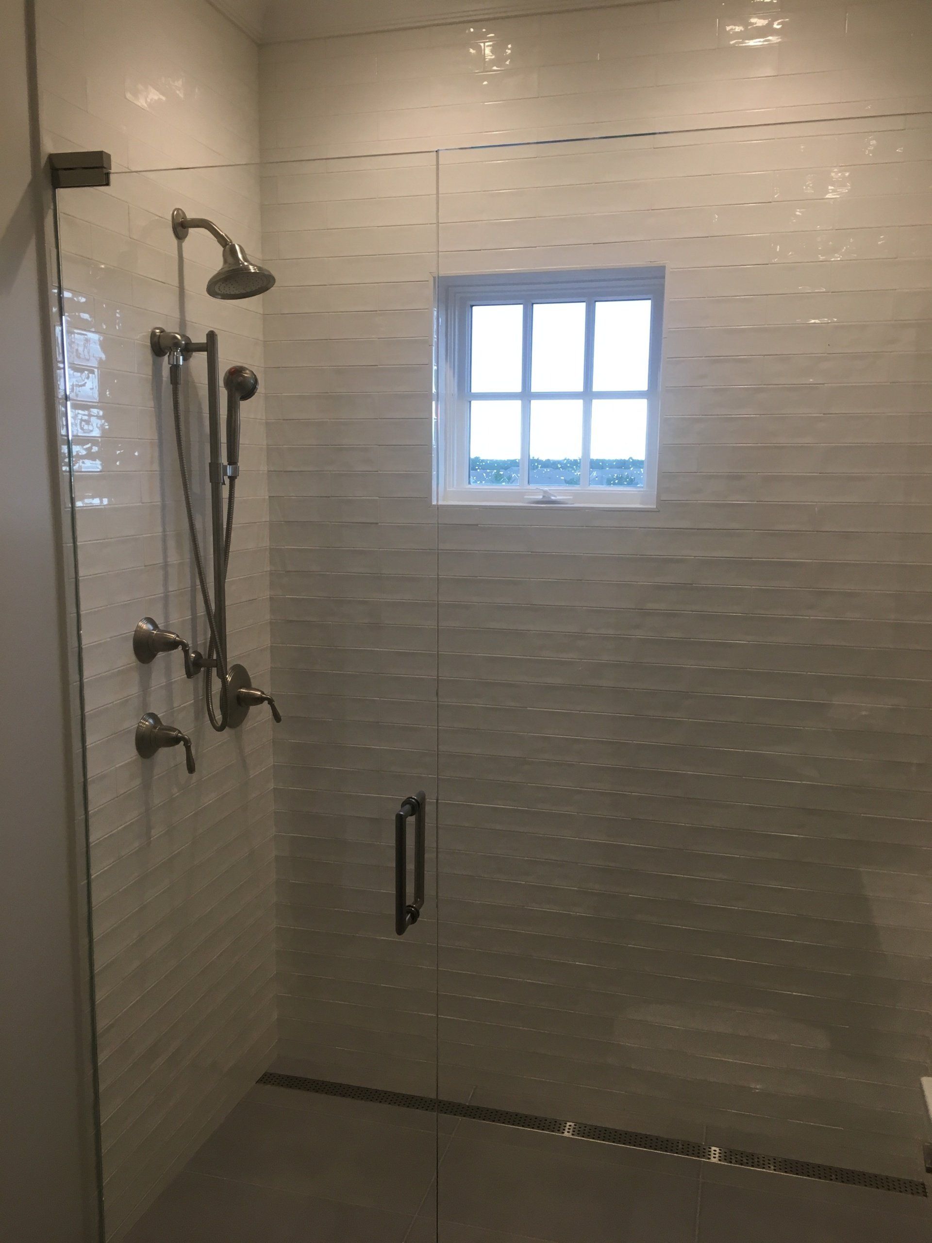 Shower with textured white wall tiles, glass door, and a small window.