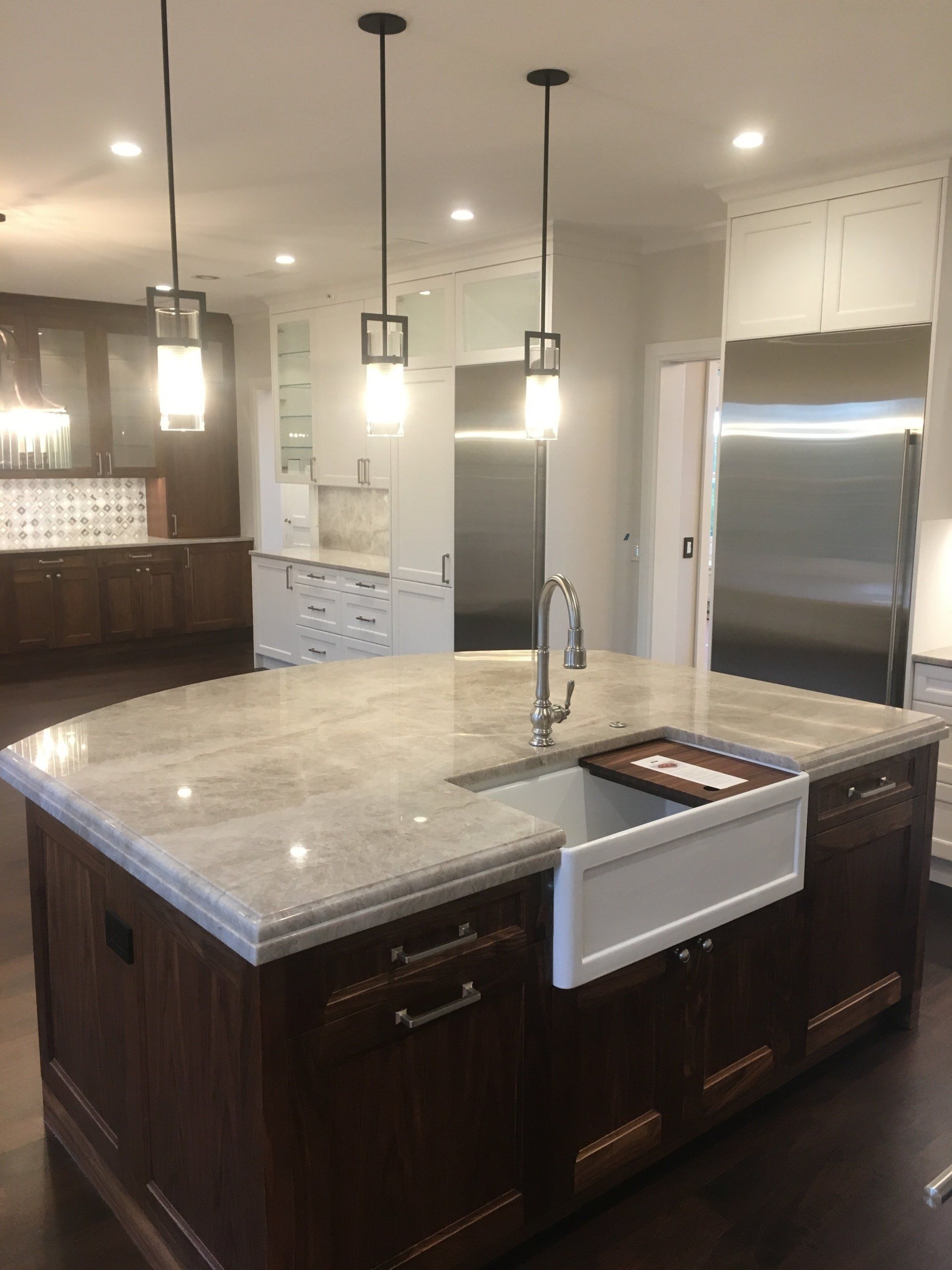Kitchen island with a white farmhouse sink, dark cabinetry, and marble countertop, with pendant lights overhead.