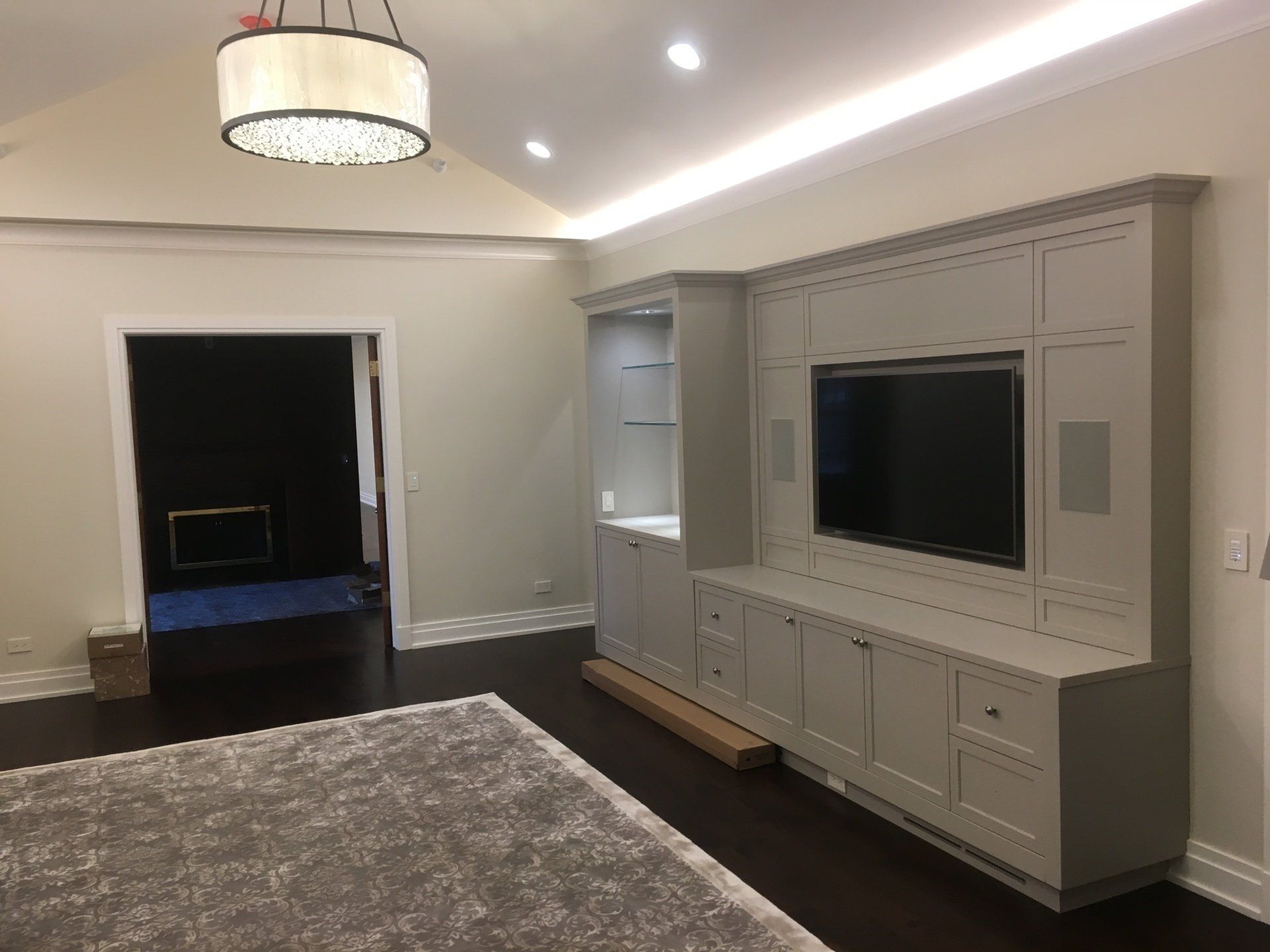 Gray media center with a TV, built-in shelves, and cabinets in a living room. Dark wood floor, light walls, and a rug.