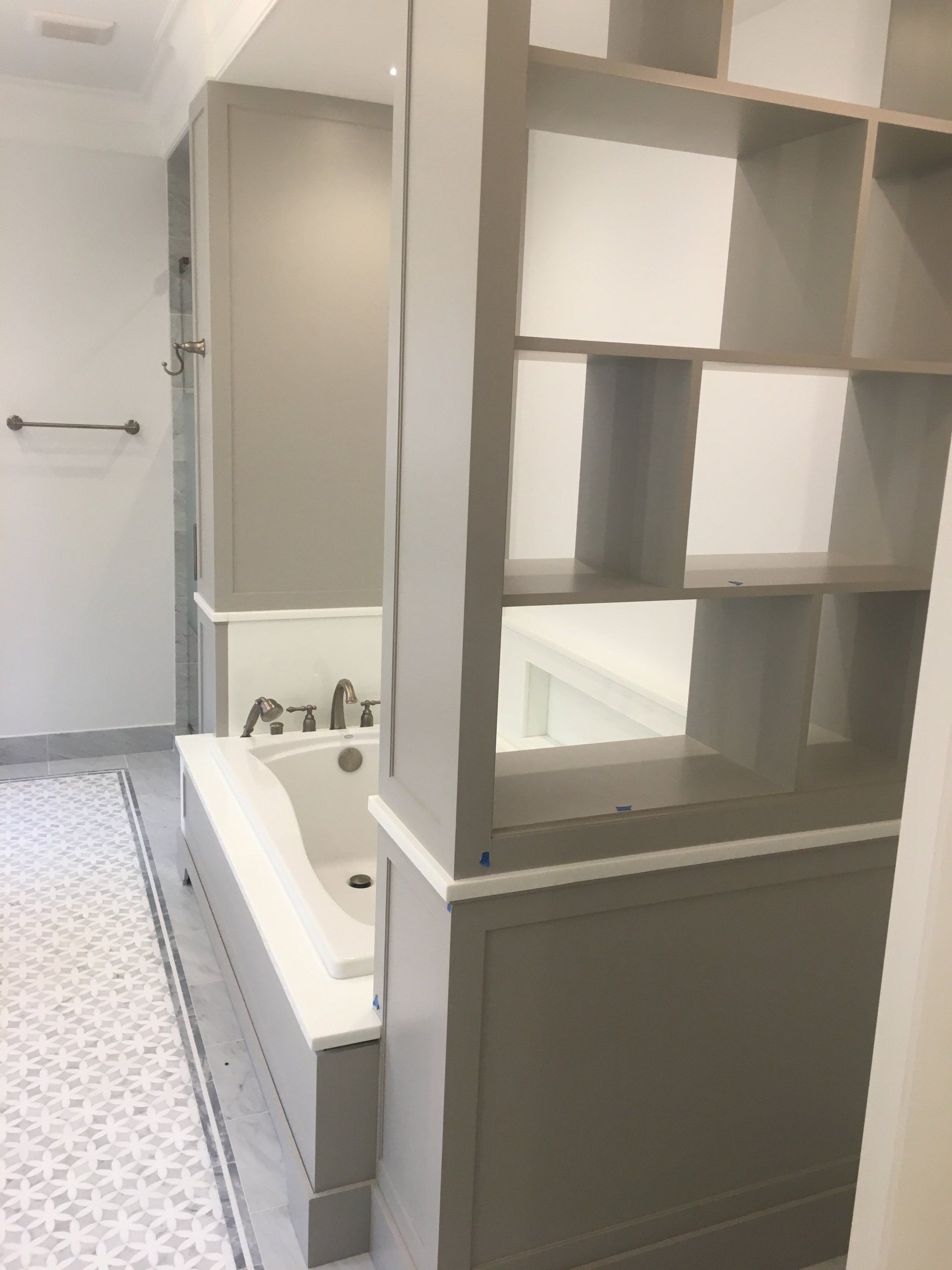 Bathroom with built-in shelving and a tub, gray and white color scheme.
