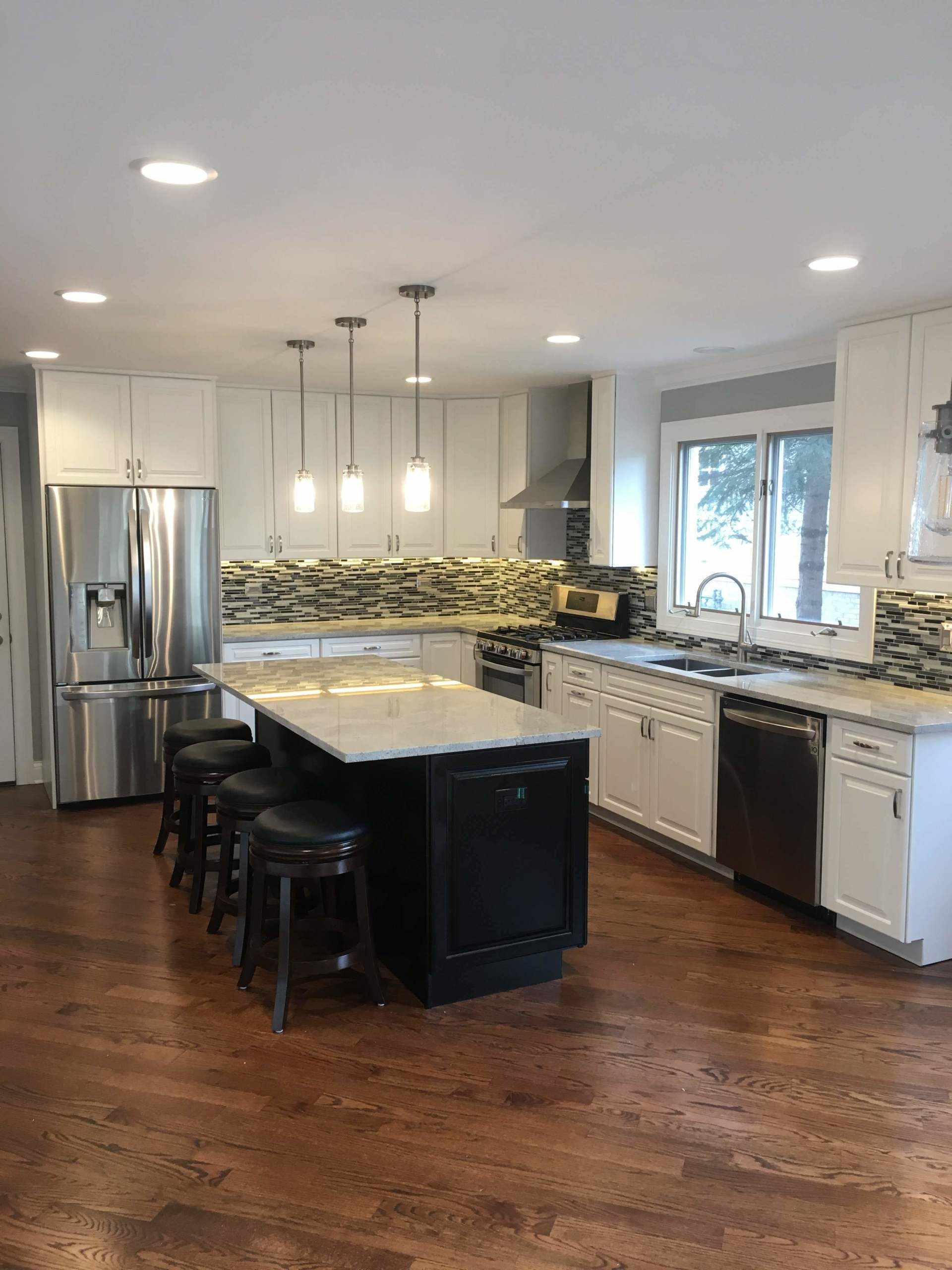 Modern kitchen with white cabinets, dark island, and stainless steel appliances.