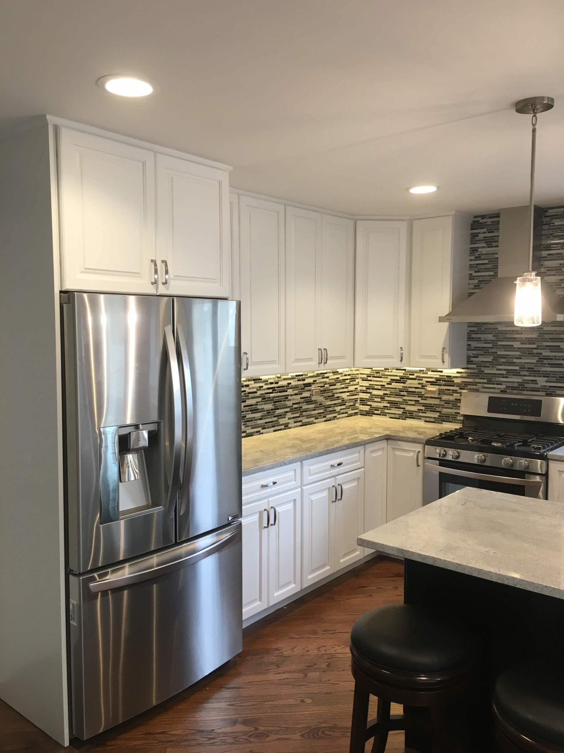 White kitchen with stainless steel fridge, cabinets, and a granite countertop.
