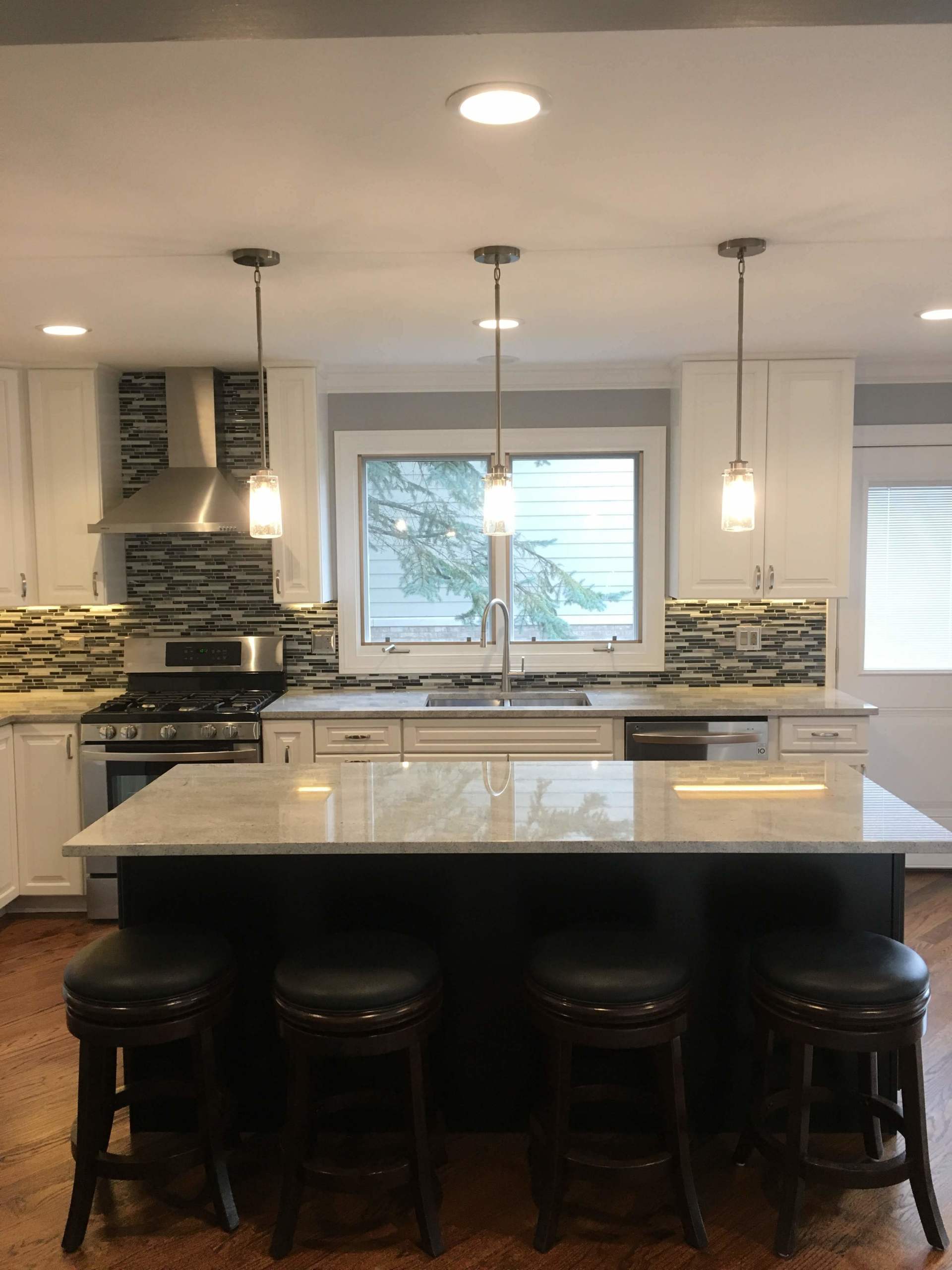 Modern kitchen with island, pendant lights, stools, and stainless steel appliances.