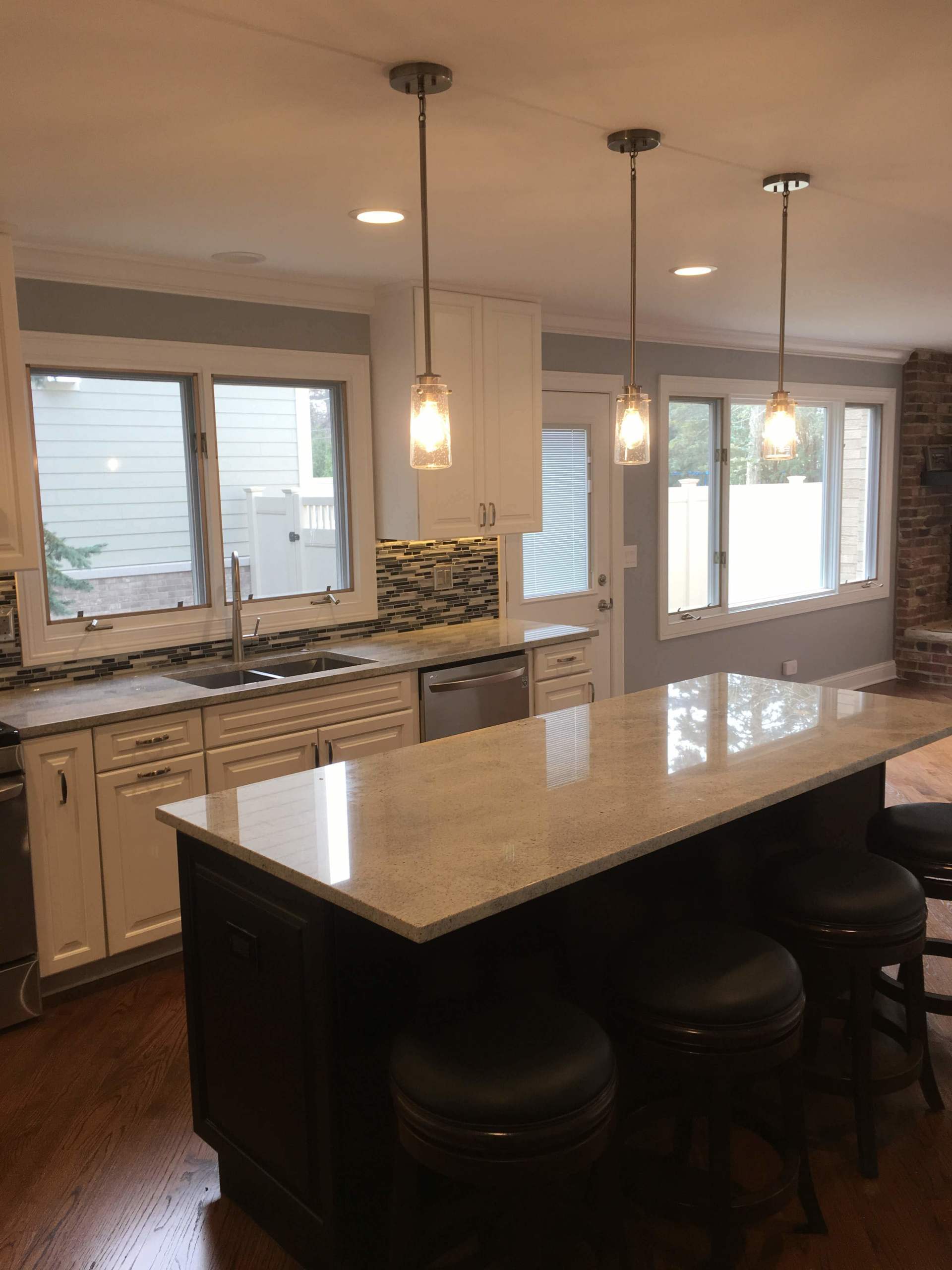 Modern kitchen with white cabinets, dark island, pendant lights, and windows.