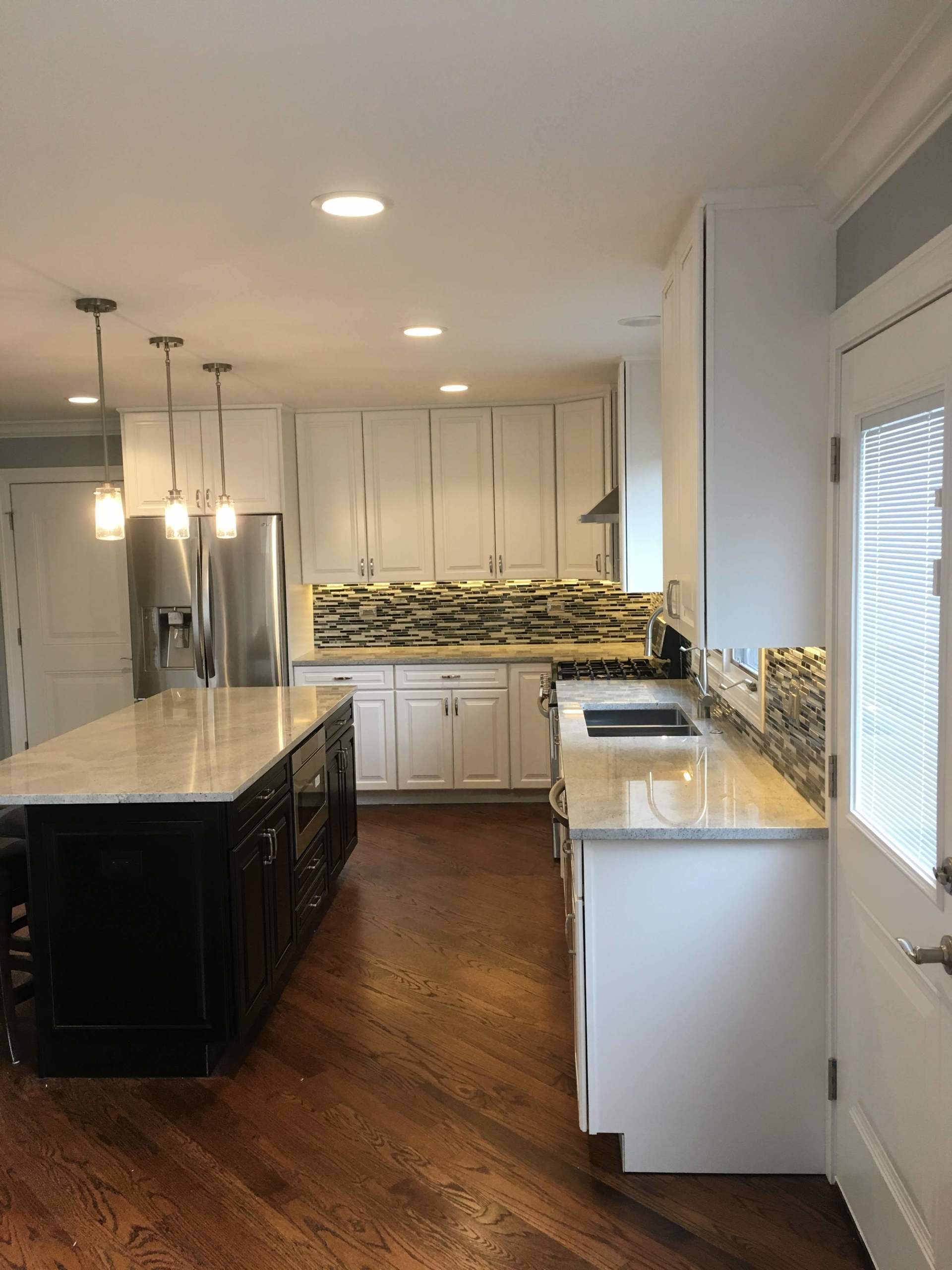 Modern kitchen with dark island and white cabinets, stainless steel appliances, and wood floors.