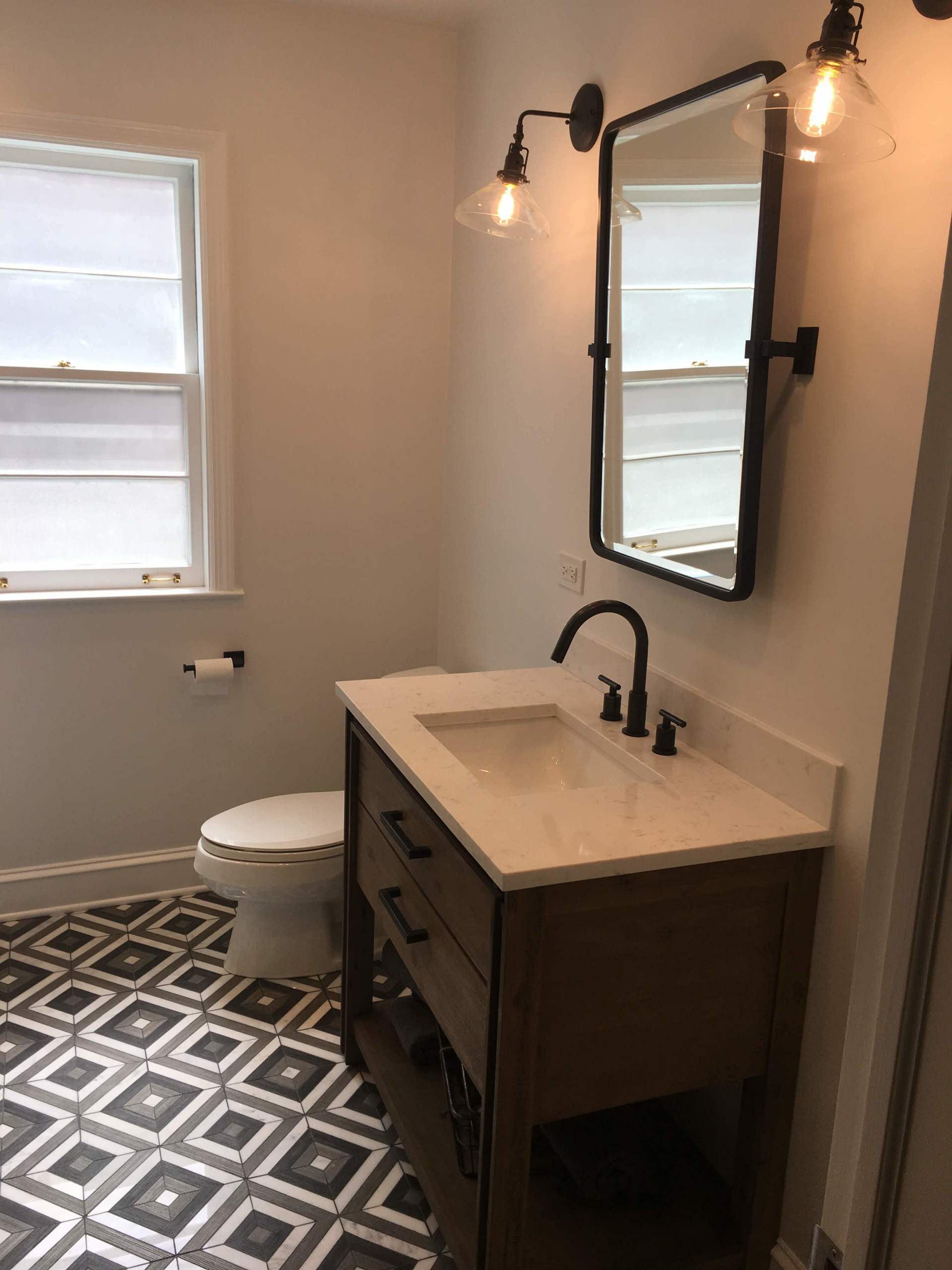 Bathroom with a dark wooden vanity, patterned floor tiles, and a black-framed mirror.