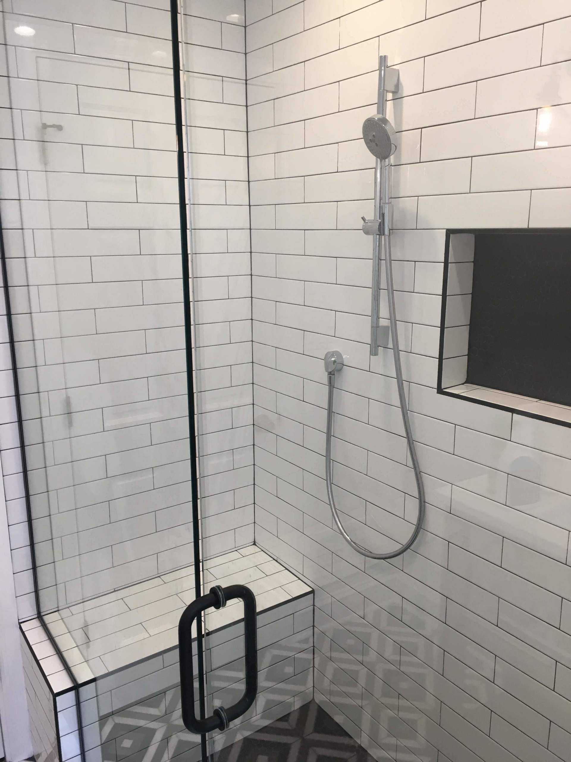 Shower with white subway tile walls, glass door, black hardware, and built-in bench and niche.