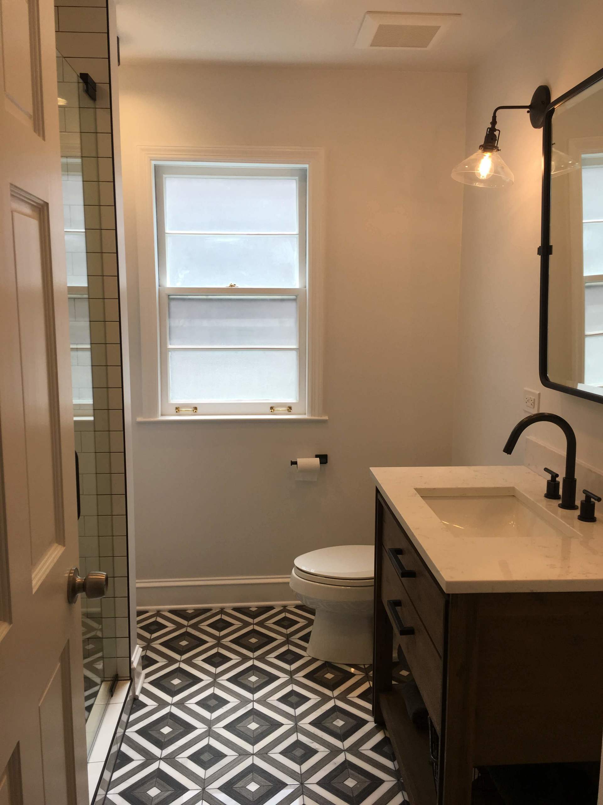 Bathroom with dark patterned floor, white walls, dark vanity, and toilet.