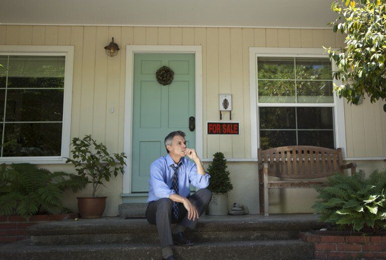 man sits in thought on porch of house