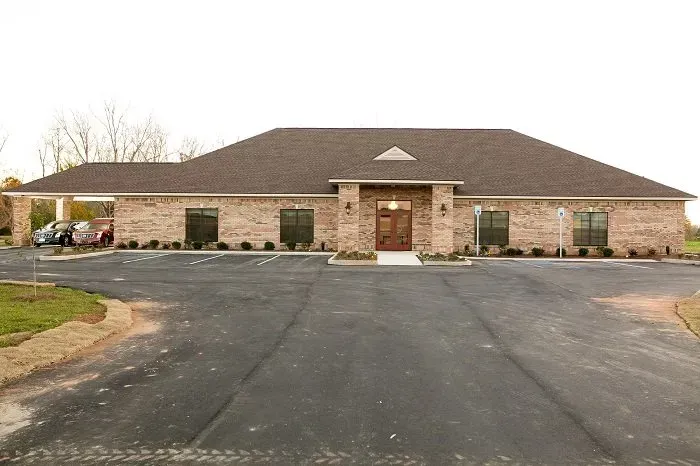 A single-story brick building with a dark shingled roof, a front entrance, and a covered driveway on the left.