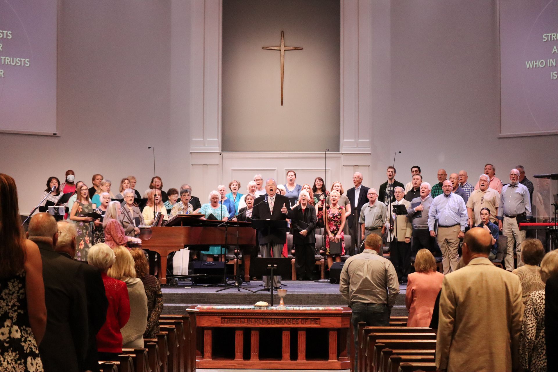 A large group of people are singing in a church with a cross in the background