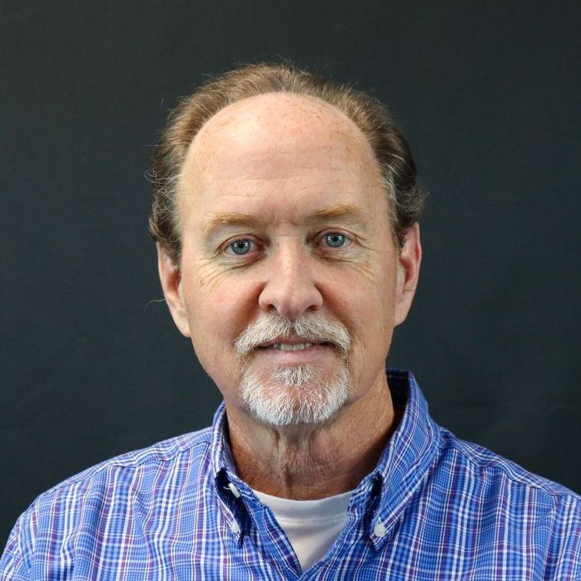 A man with a beard is wearing a blue plaid shirt.