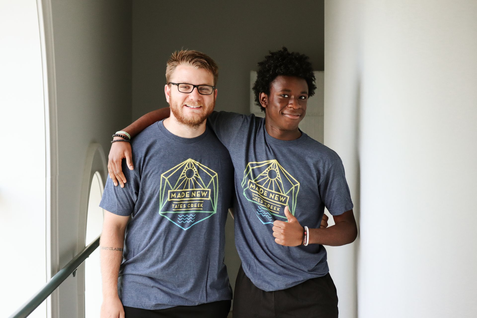Two men are standing next to each other in a hallway and one of them is giving a thumbs up.
