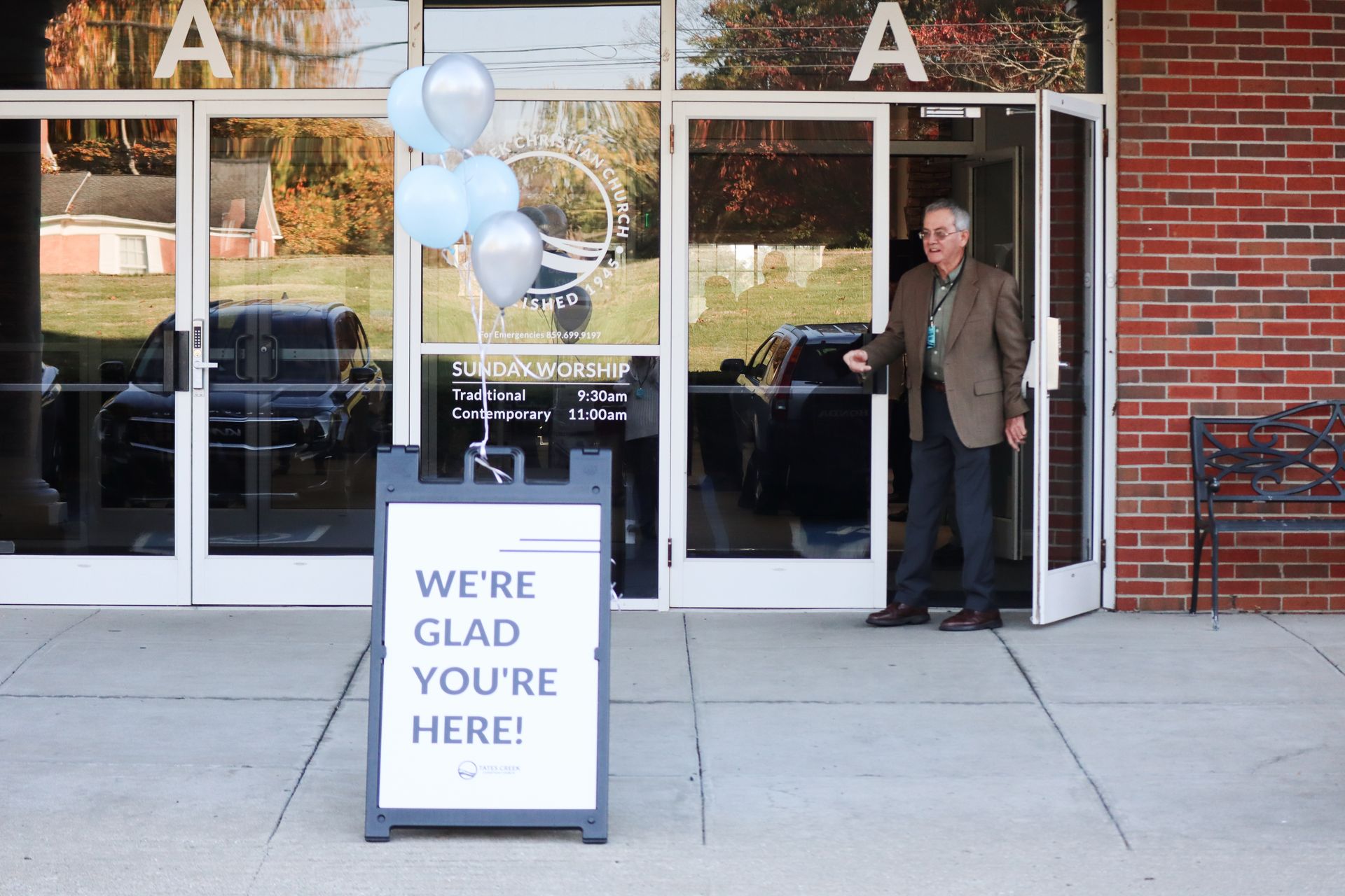 A man is standing in front of a building with a sign that says we 're glad you 're here