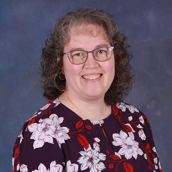 A woman wearing glasses and a purple shirt is smiling.