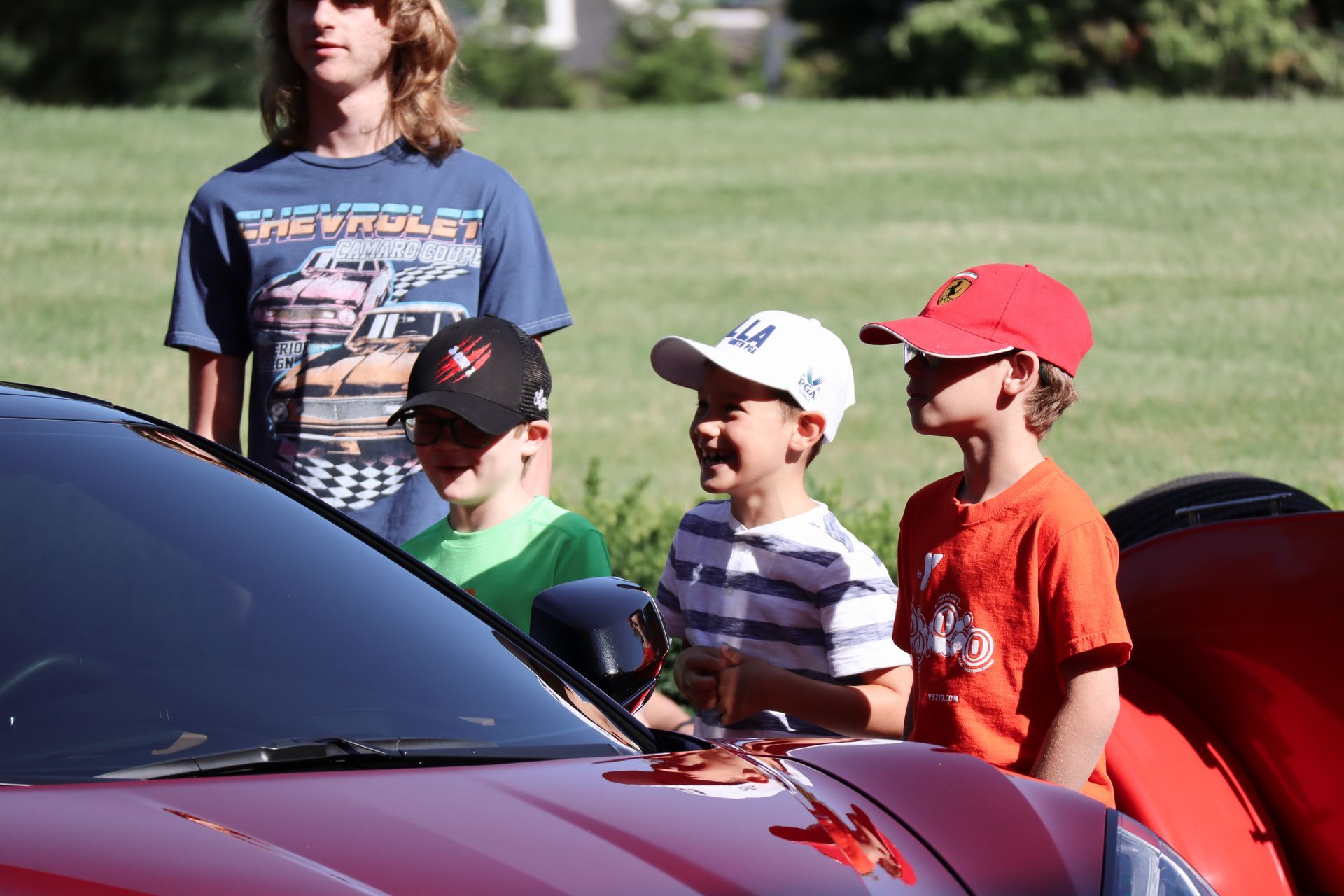 A group of young boys are standing around a red chevrolet car