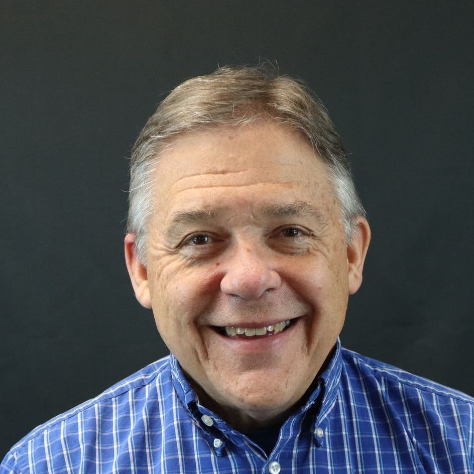 A man in a blue plaid shirt is smiling for the camera.