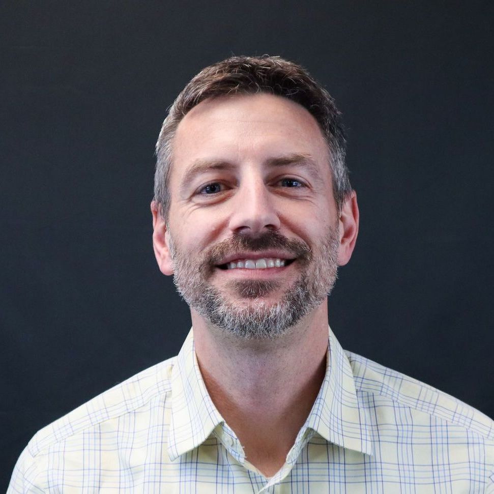 A man with a beard is smiling for the camera while wearing a plaid shirt.