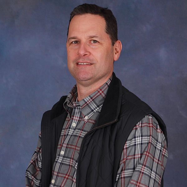A man with dark hair and a plaid shirt is smiling for the camera.