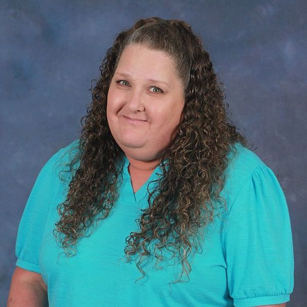 A woman with curly hair is wearing a blue shirt and smiling.