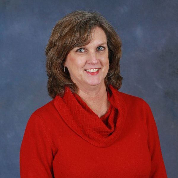 A woman wearing a gray shirt and a necklace is smiling for the camera.