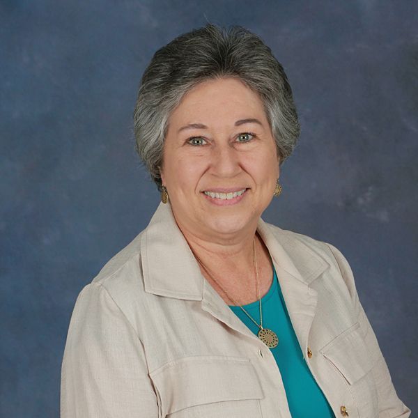 A woman wearing a gray sweater and a black shirt is smiling for the camera.