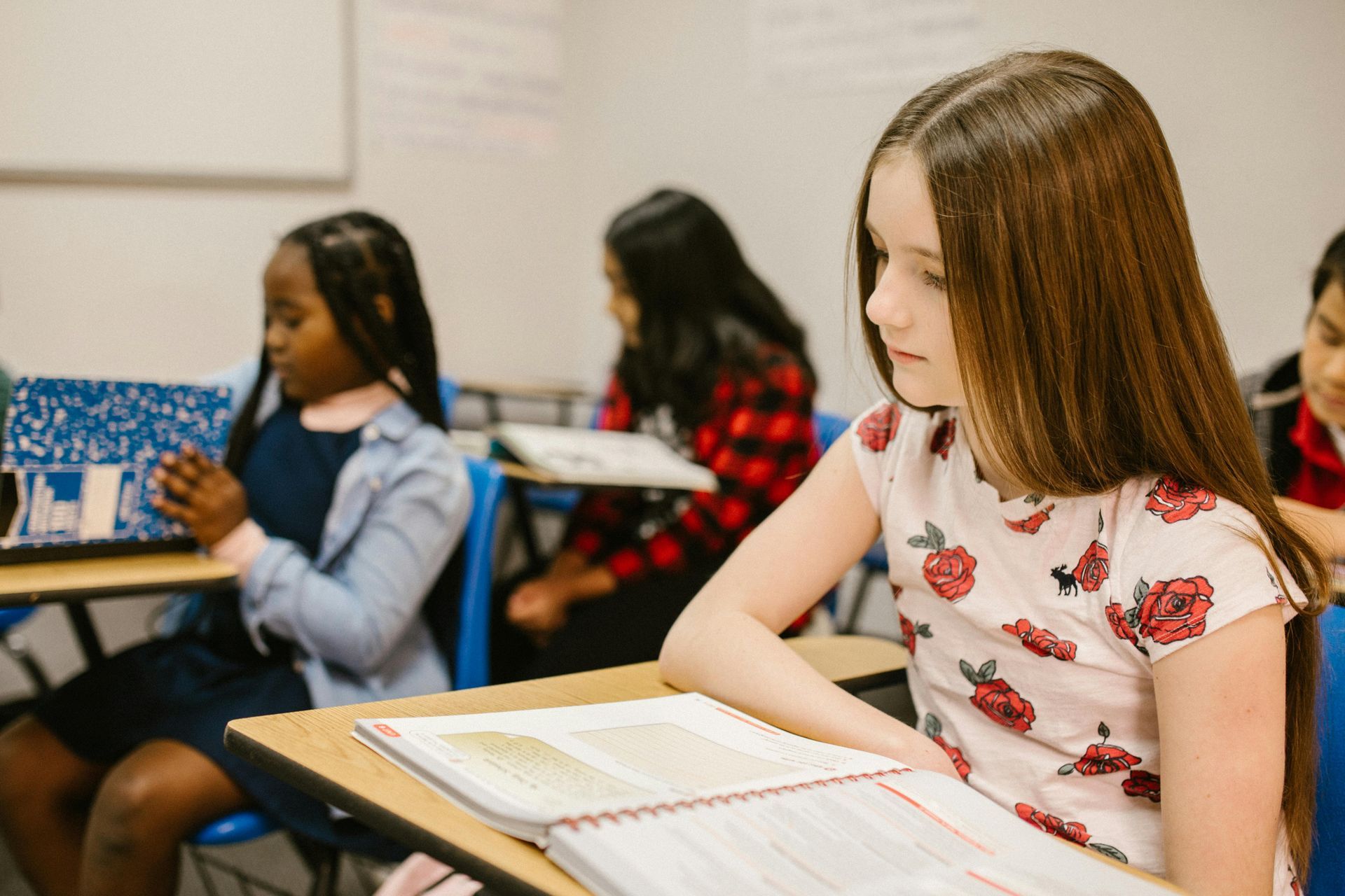 A girl is sitting at a desk in a classroom reading a book.